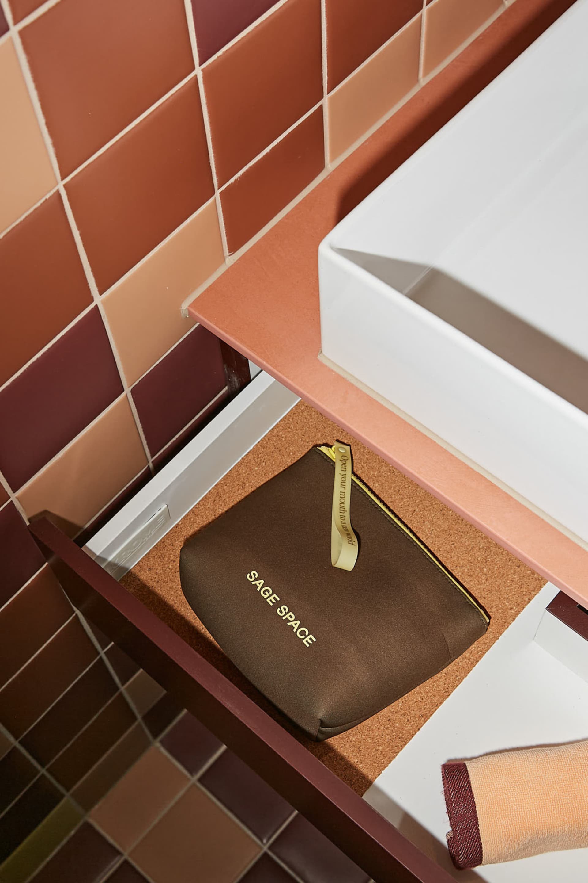 A brown Sage Space pouch with a gold ribbon on a countertop.