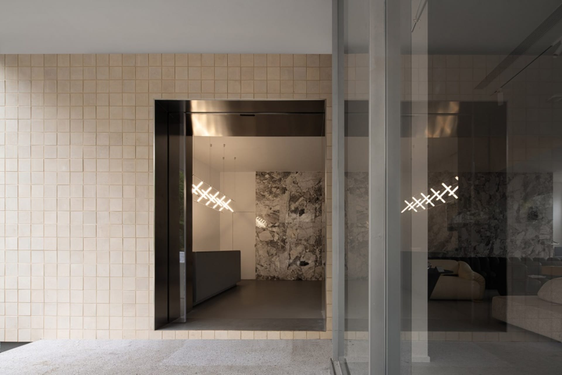 A modern industrial lobby with concrete and tile walls, featuring a minimalist design with geometric lighting fixtures.