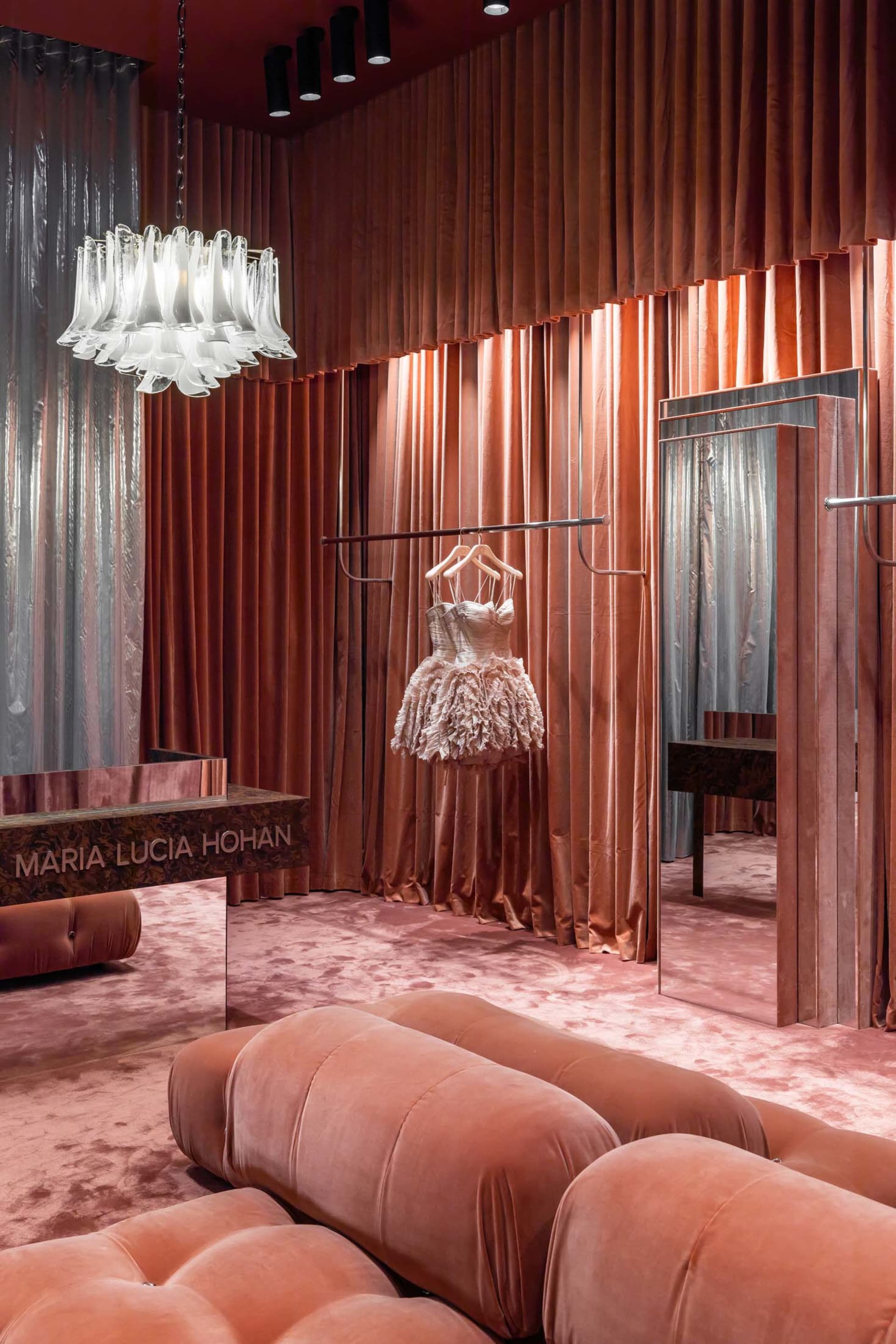 A luxurious retail shop with velvet curtains, a leather sofa, and a velvet dress hanging on a metal rack