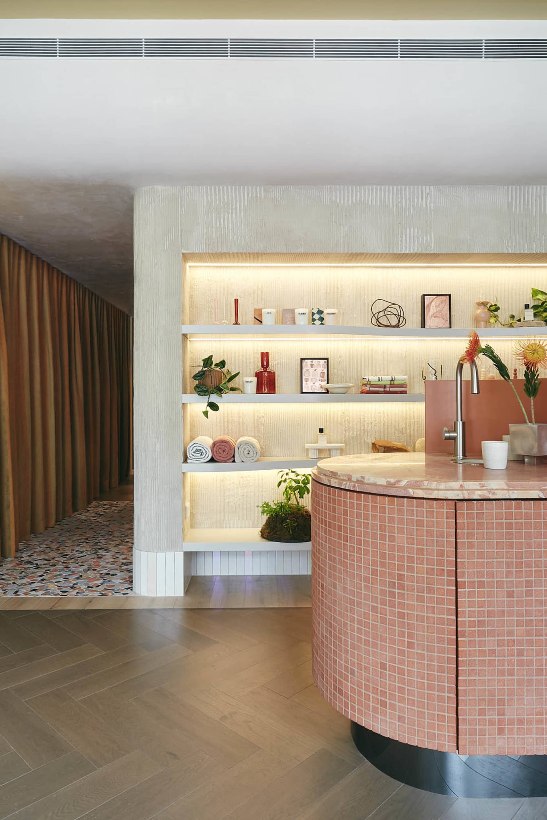 A spa interior featuring terrazzo countertops and marble accents, with a circular counter, shelves displaying spa products, a