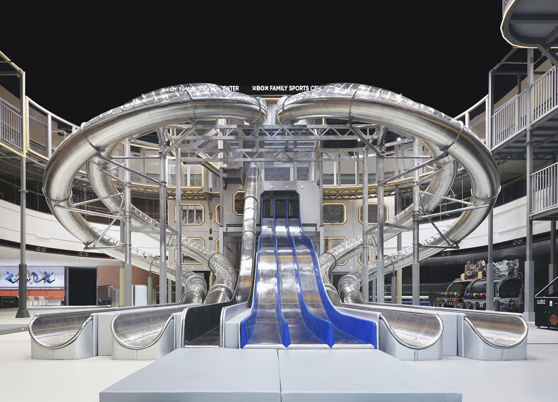 A large, indoor playground featuring a metal spiral slide and a series of tubes connected by a central structure.