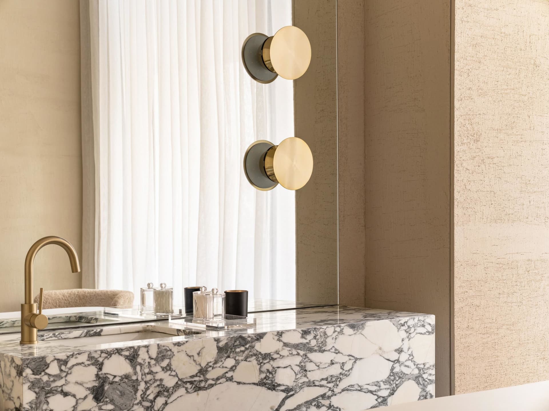 A modern bathroom featuring a marble countertop with a sink and faucet, accompanied by two wall-mounted light fixtures with r