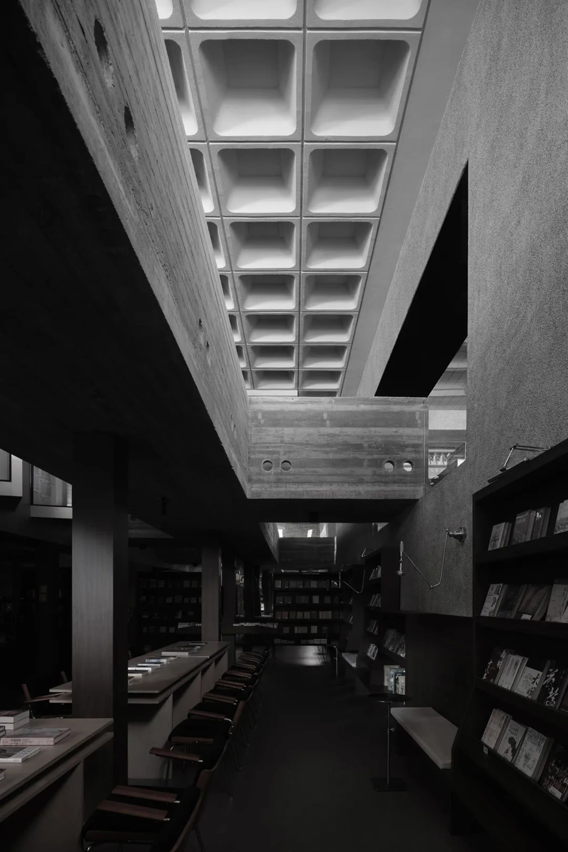 一張黑白照片,展示現代圖書館室內空間,混凝土牆面搭配格柵天花板。