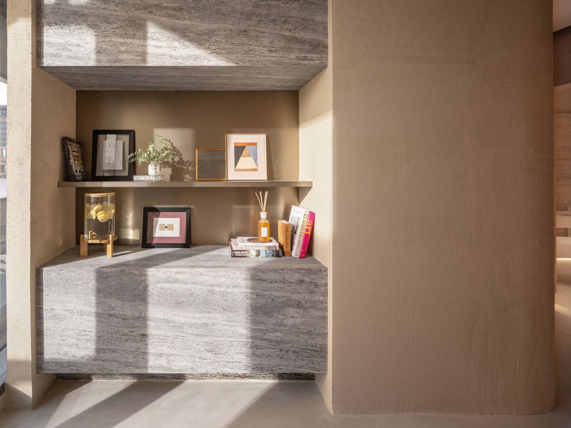 A modern interior space featuring concrete and plaster walls and shelves with framed pictures and books.