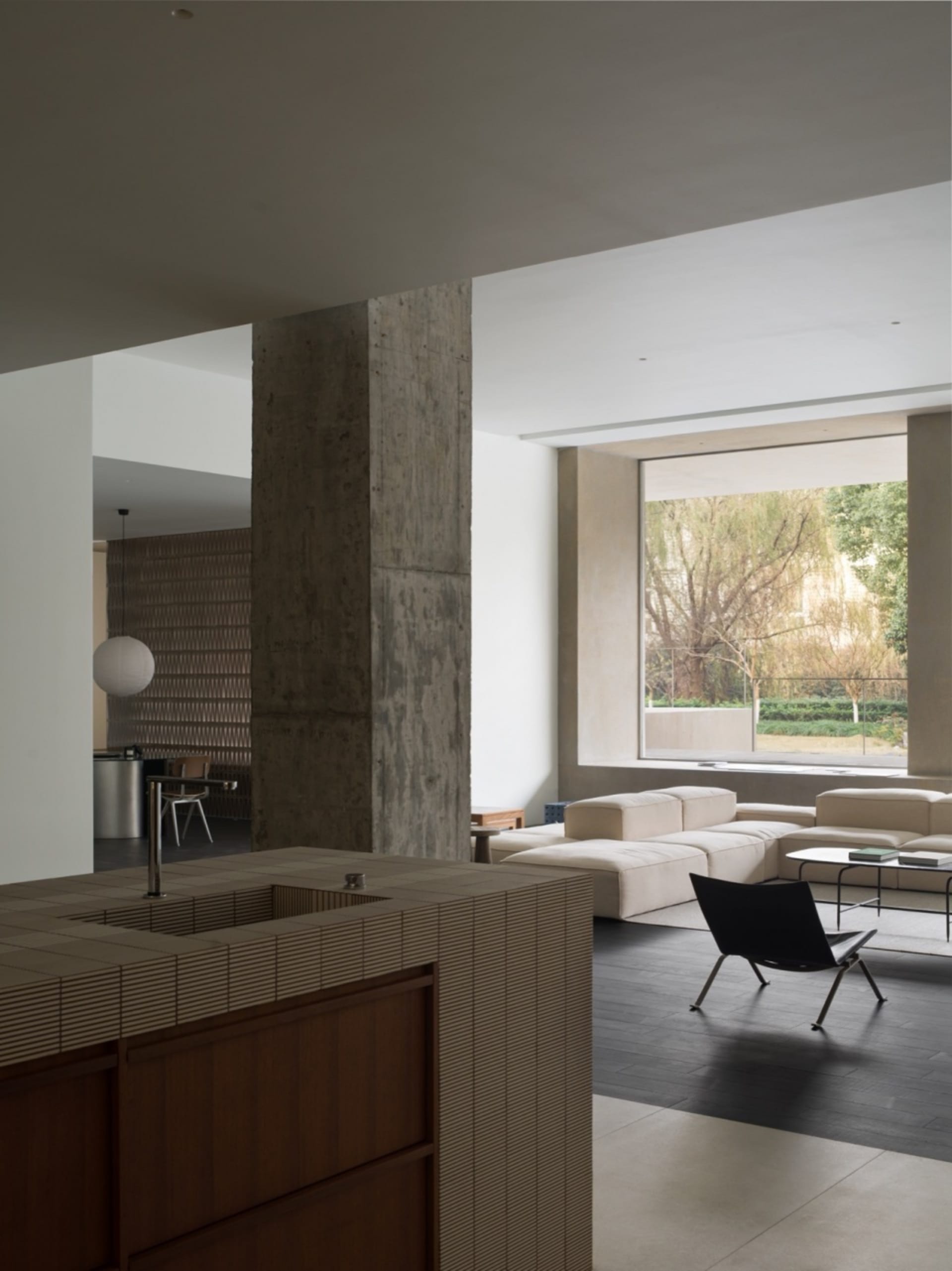 Modern minimalist living room with exposed concrete columns and large windows.