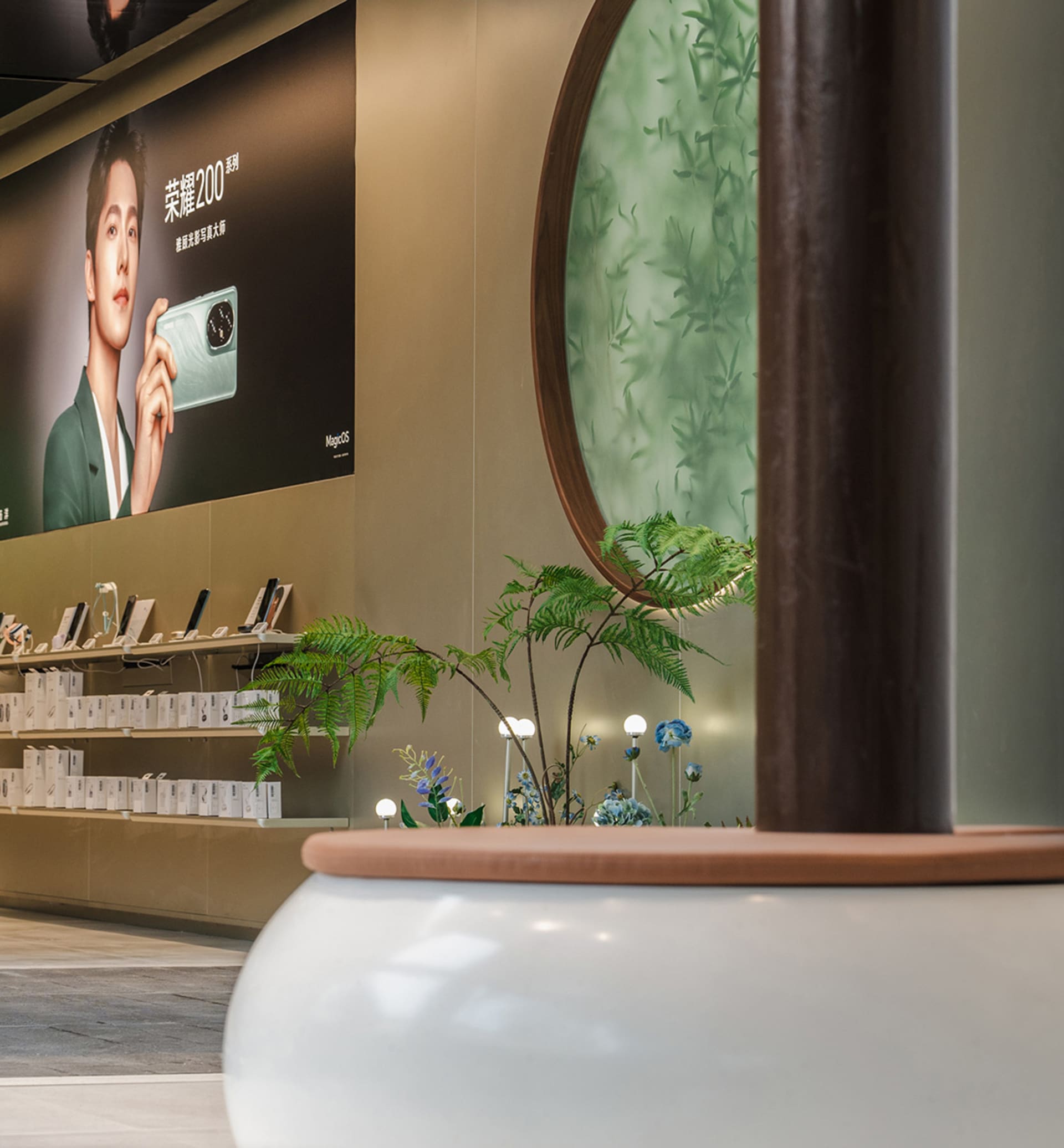 A modern retail store featuring minimalist design with green plants, shelves displaying electronic devices, and a circular gl