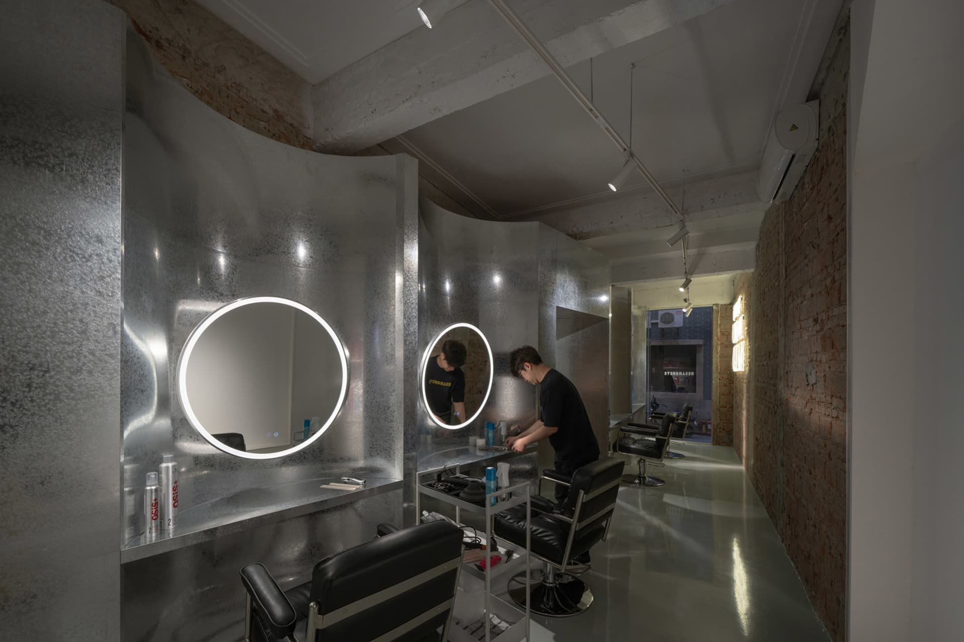 A modern barber shop featuring metallic finishes, industrial lighting, and illuminated circular mirrors.