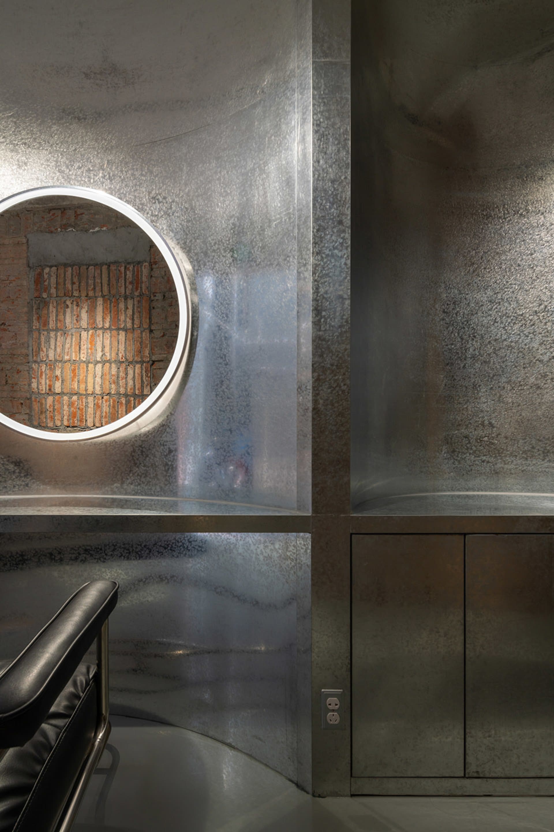 A modern industrial-style watering station made of metal, featuring a small circular window and a minimalist design.