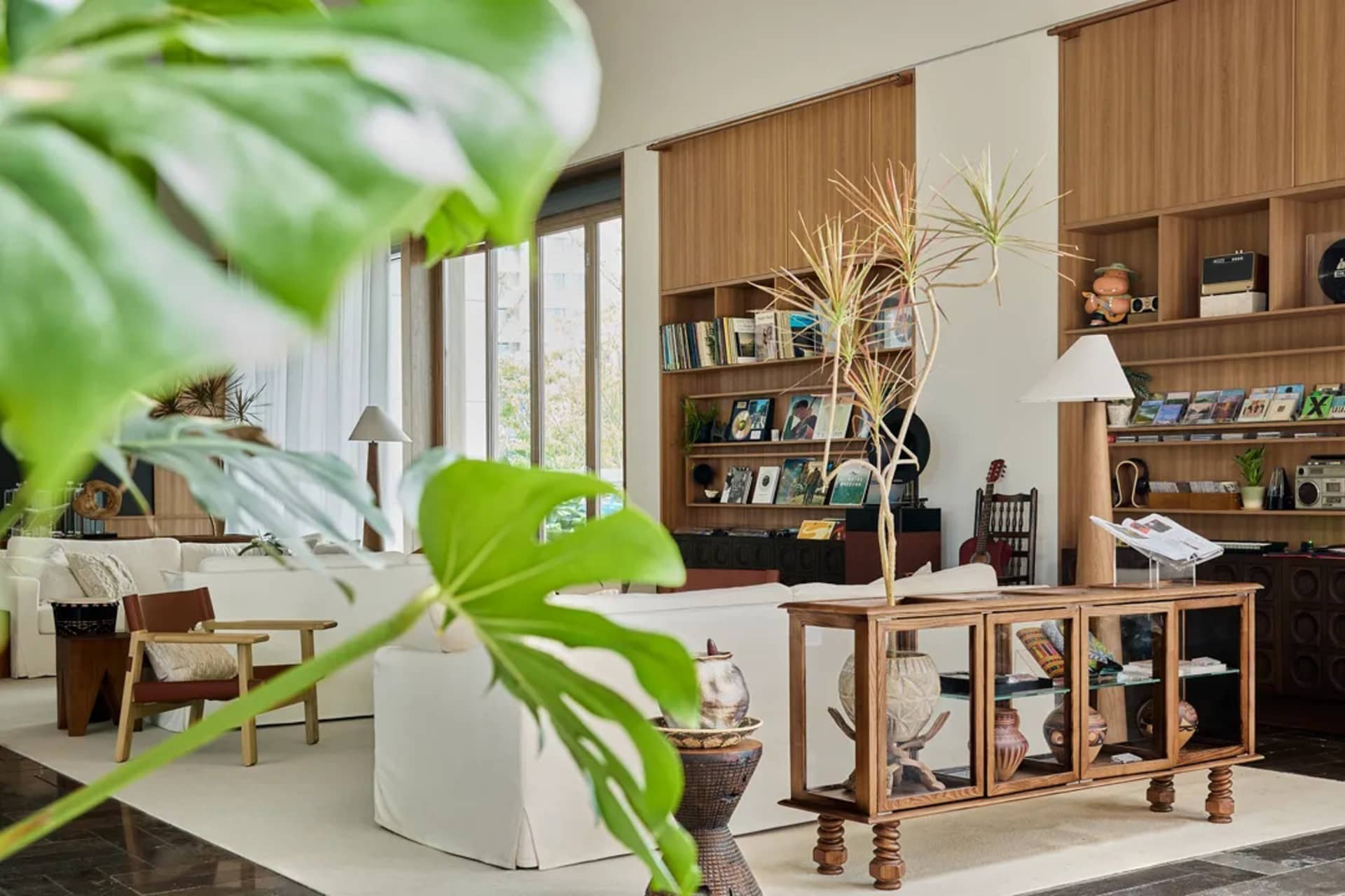 A modern minimalist living room with wooden furniture, glass shelving, and leather sofas.