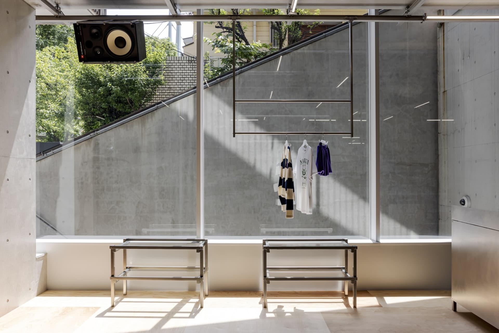 A minimalist retail space featuring concrete walls, metal clothing racks, and hanging clothing.