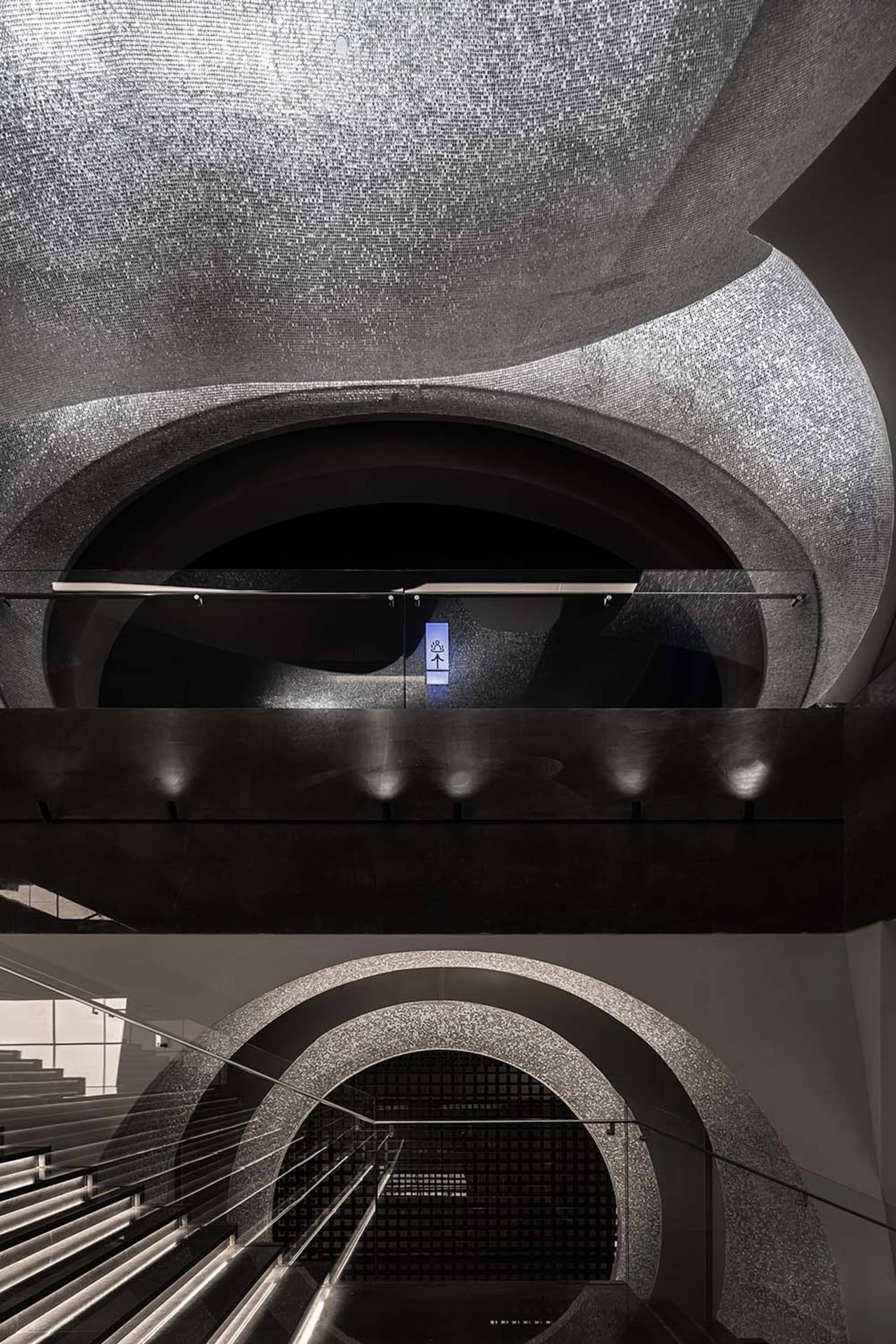Luxurious modern interior with glass mosaic floor, stone archways, and metallic railings.