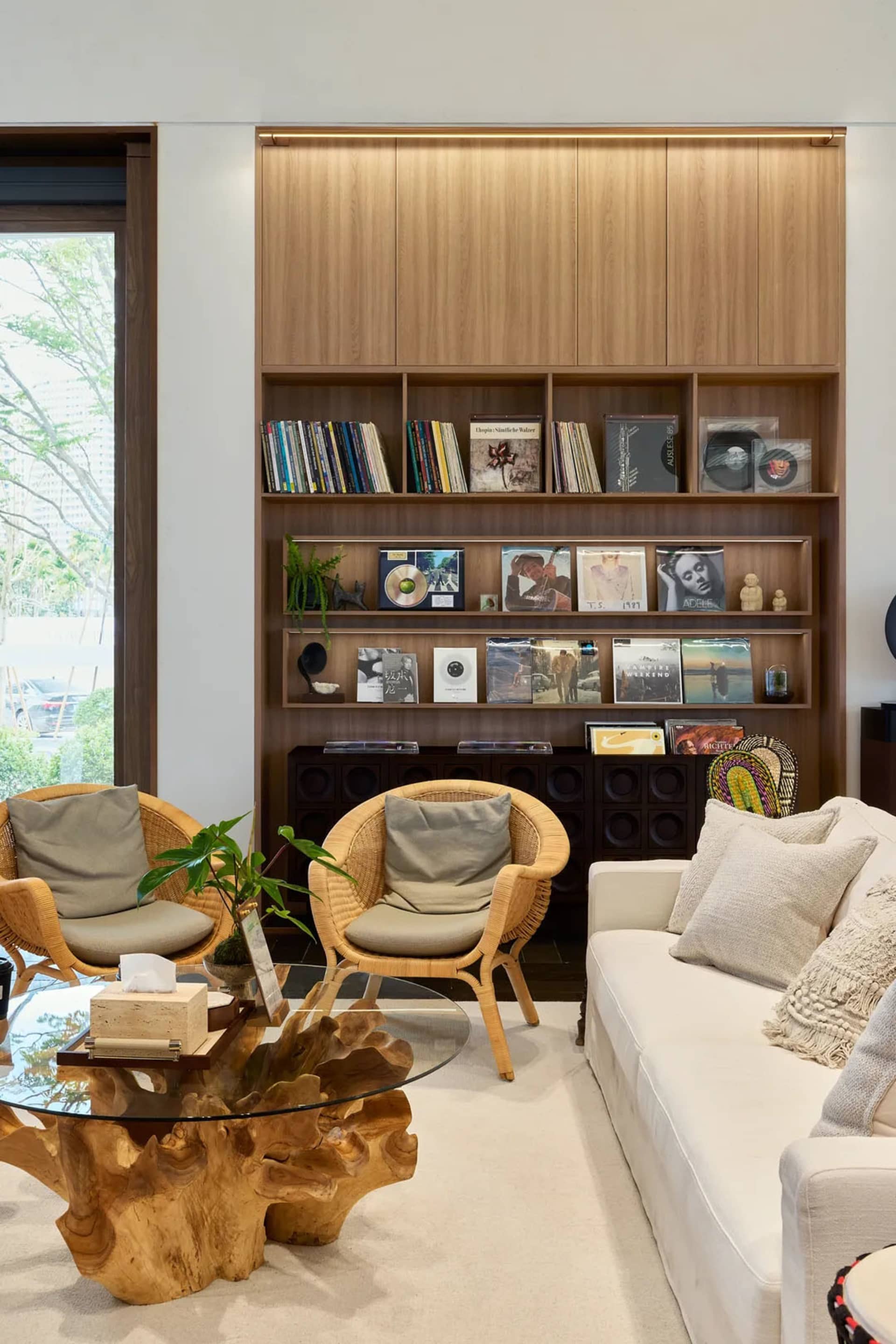 Modern living room featuring a white sofa and two rattan armchairs arranged around a glass coffee table, with a large bookshe