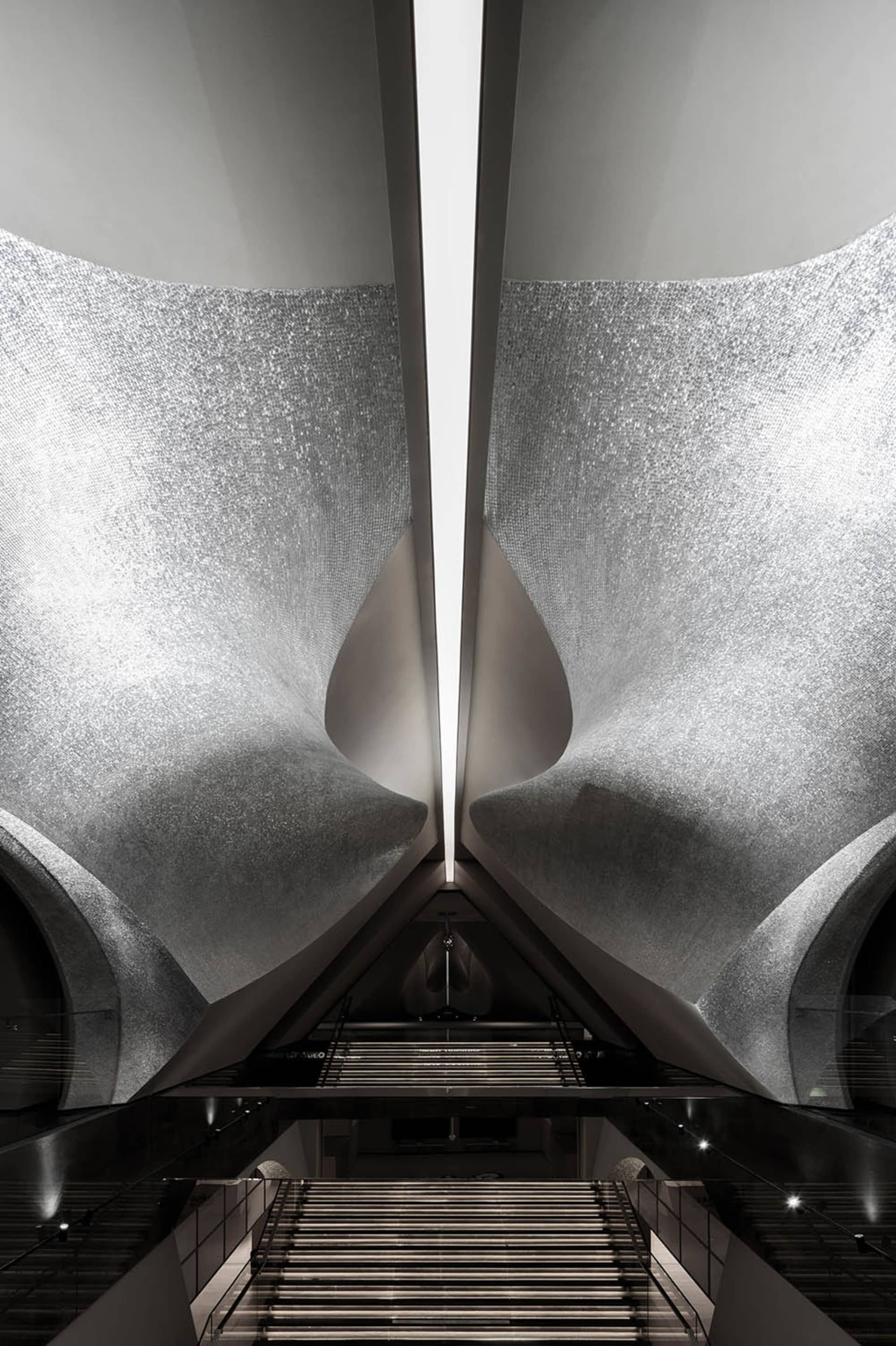 A futuristic, spacious transportation station with metallic walls reflecting light and a staircase leading downwards.