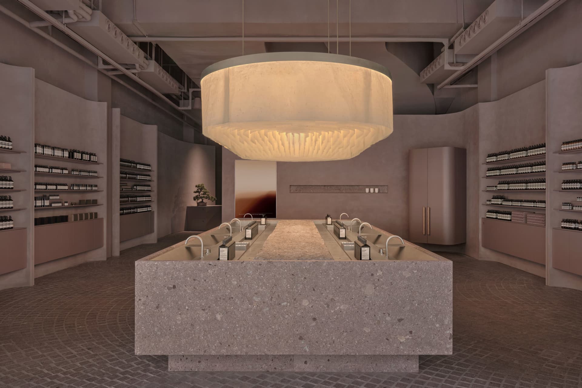 Modern retail shop with concrete and terrazzo furniture, featuring a central island with multiple sinks and bottles of produc