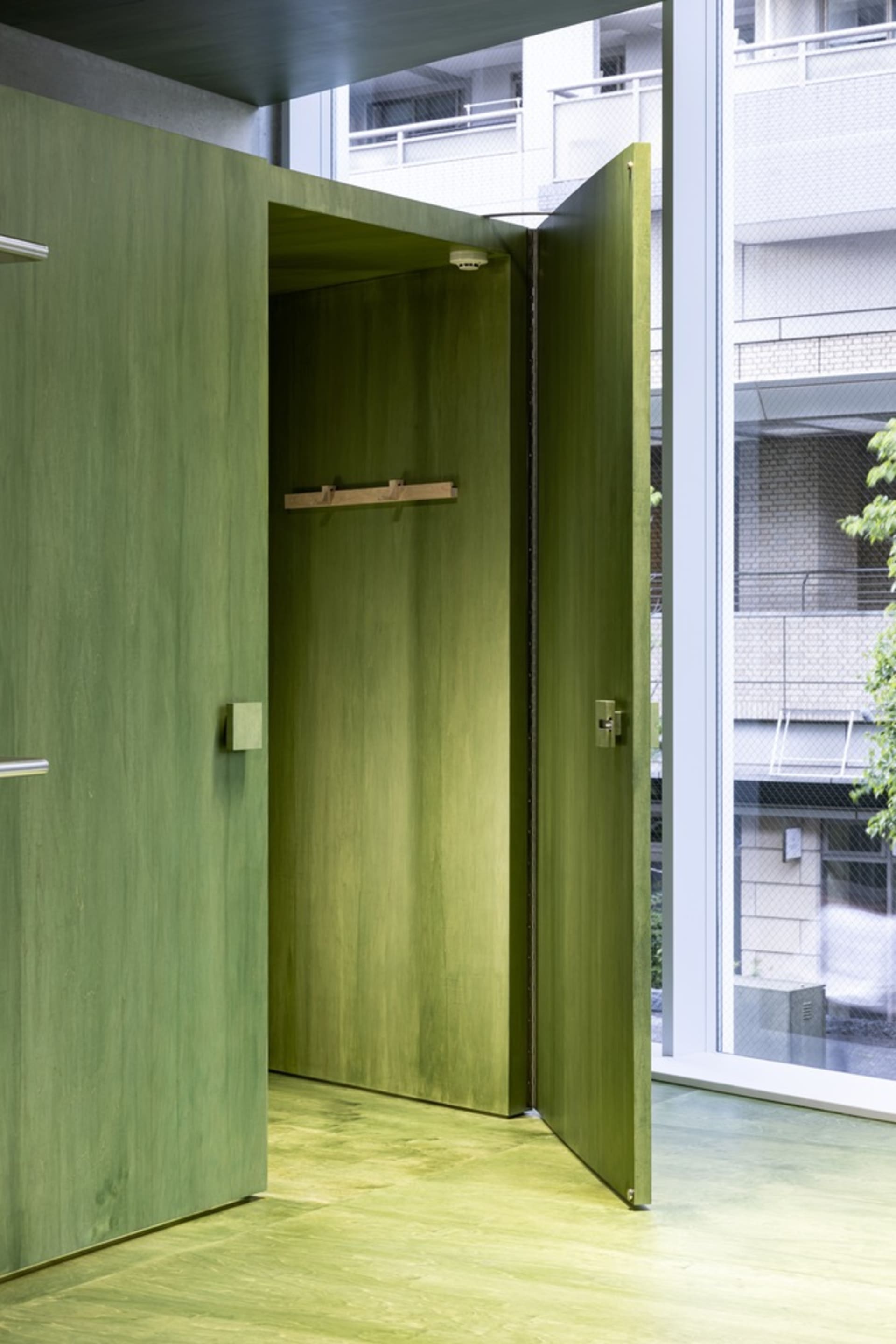 An open green wooden door in an industrial-style interior space, featuring green flooring and walls.