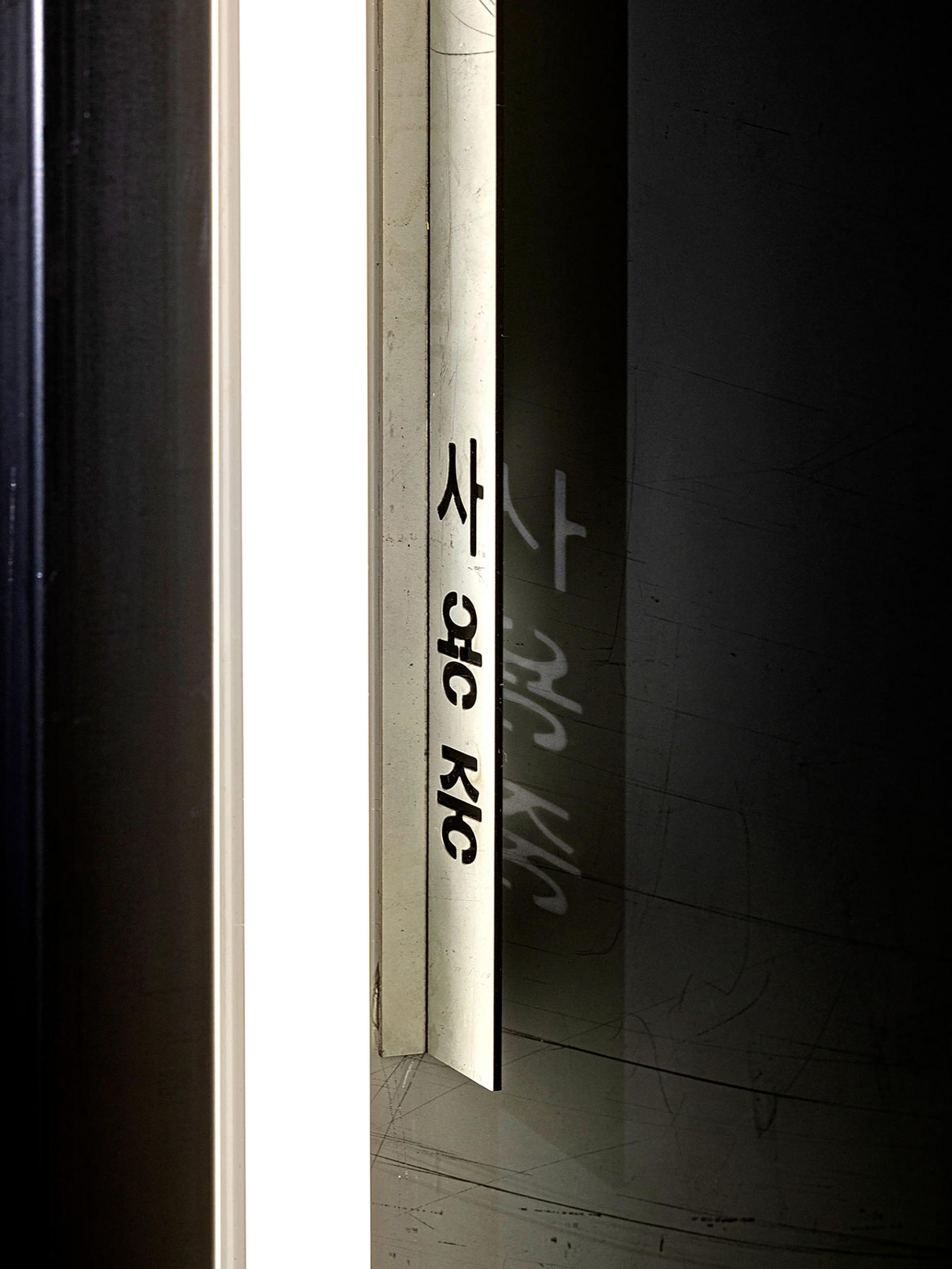Metal door with Korean text on the edge, illuminated by light from the door's other side.