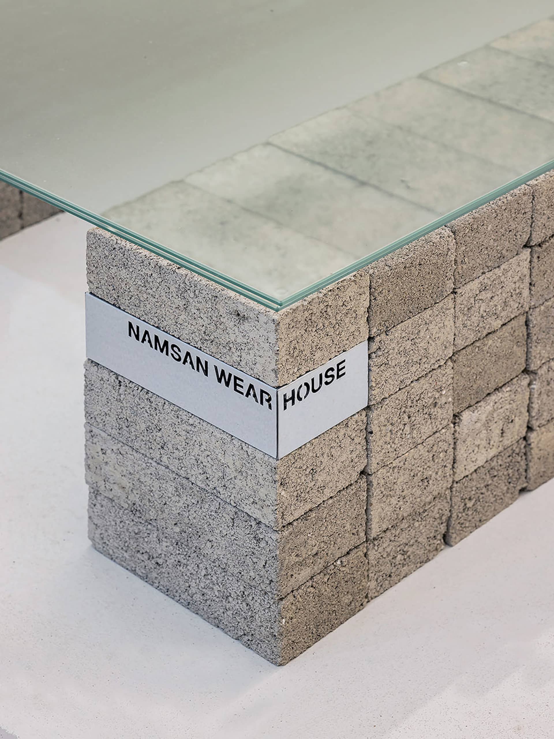 A minimalist desk with a glass top and a base made of stacked concrete blocks.