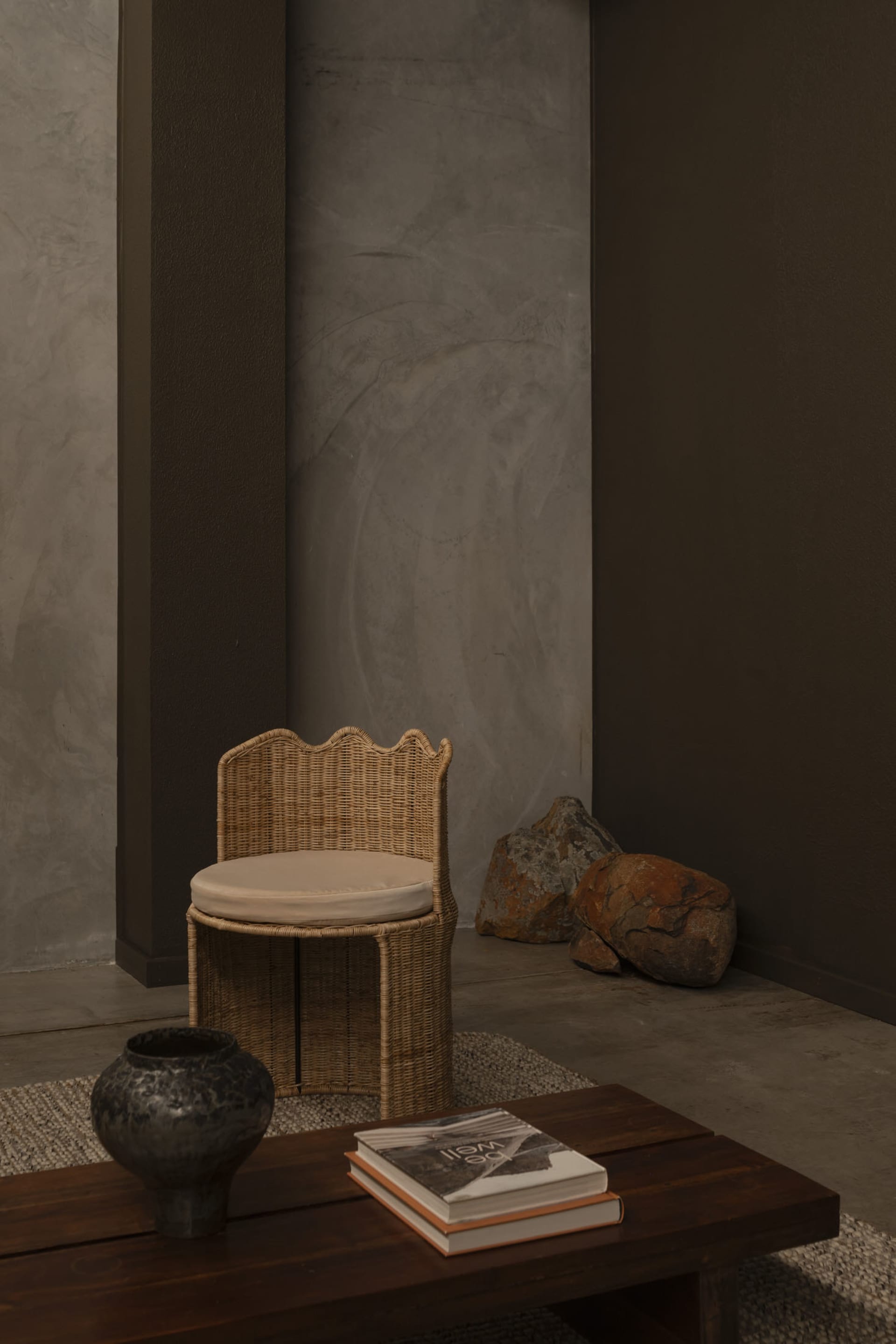 A minimalist living room with a wicker chair and a table with books and a vase on it.