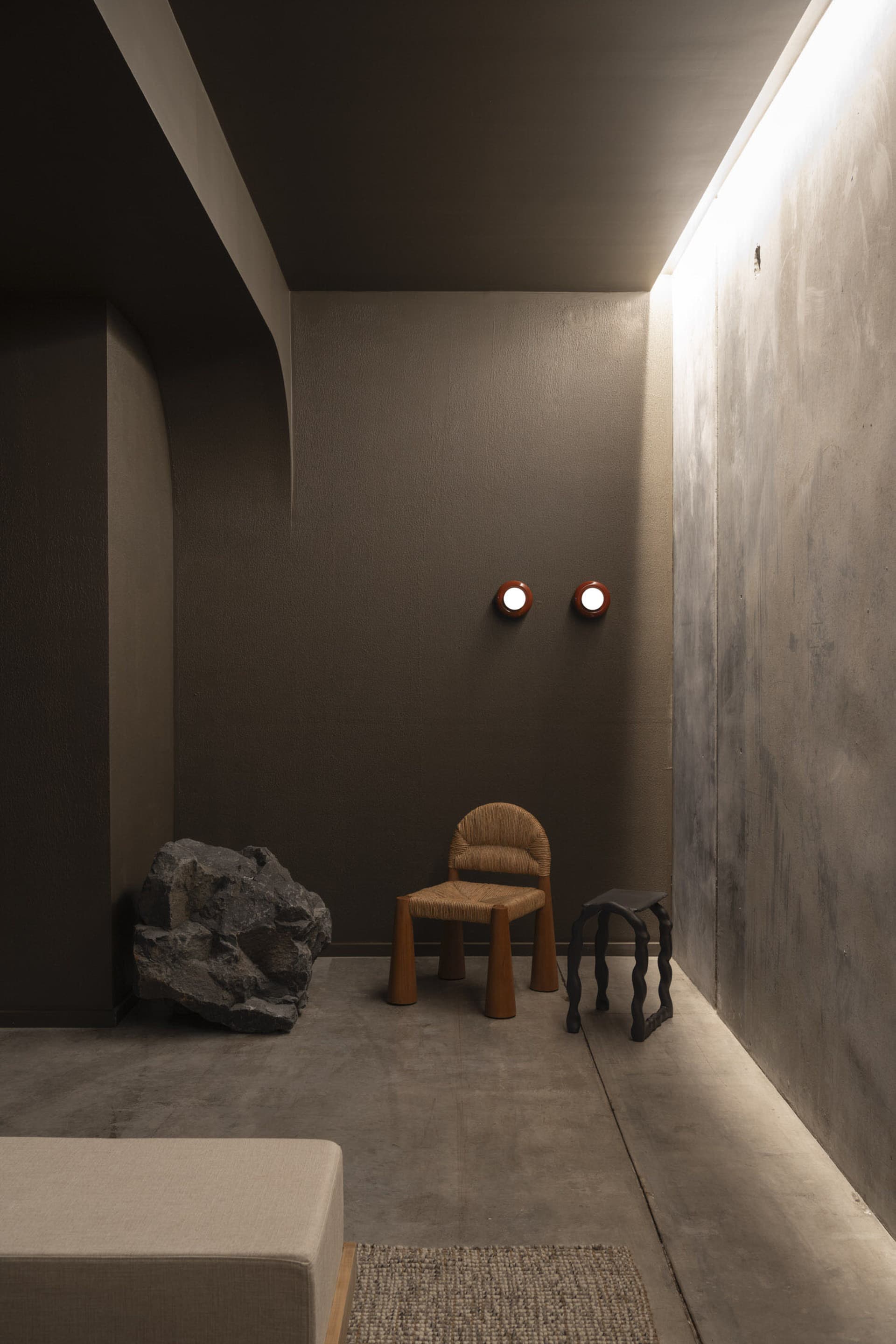 A minimalist living space featuring concrete walls and wood furniture.