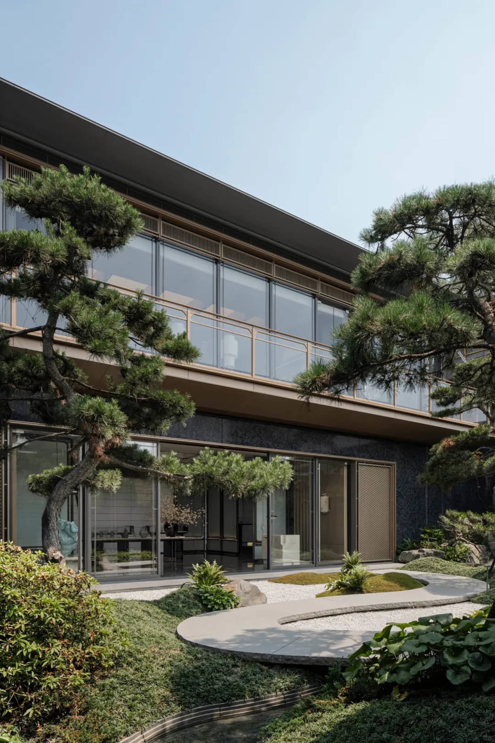 Modern residential exterior with glass walls, concrete floor, and pine trees