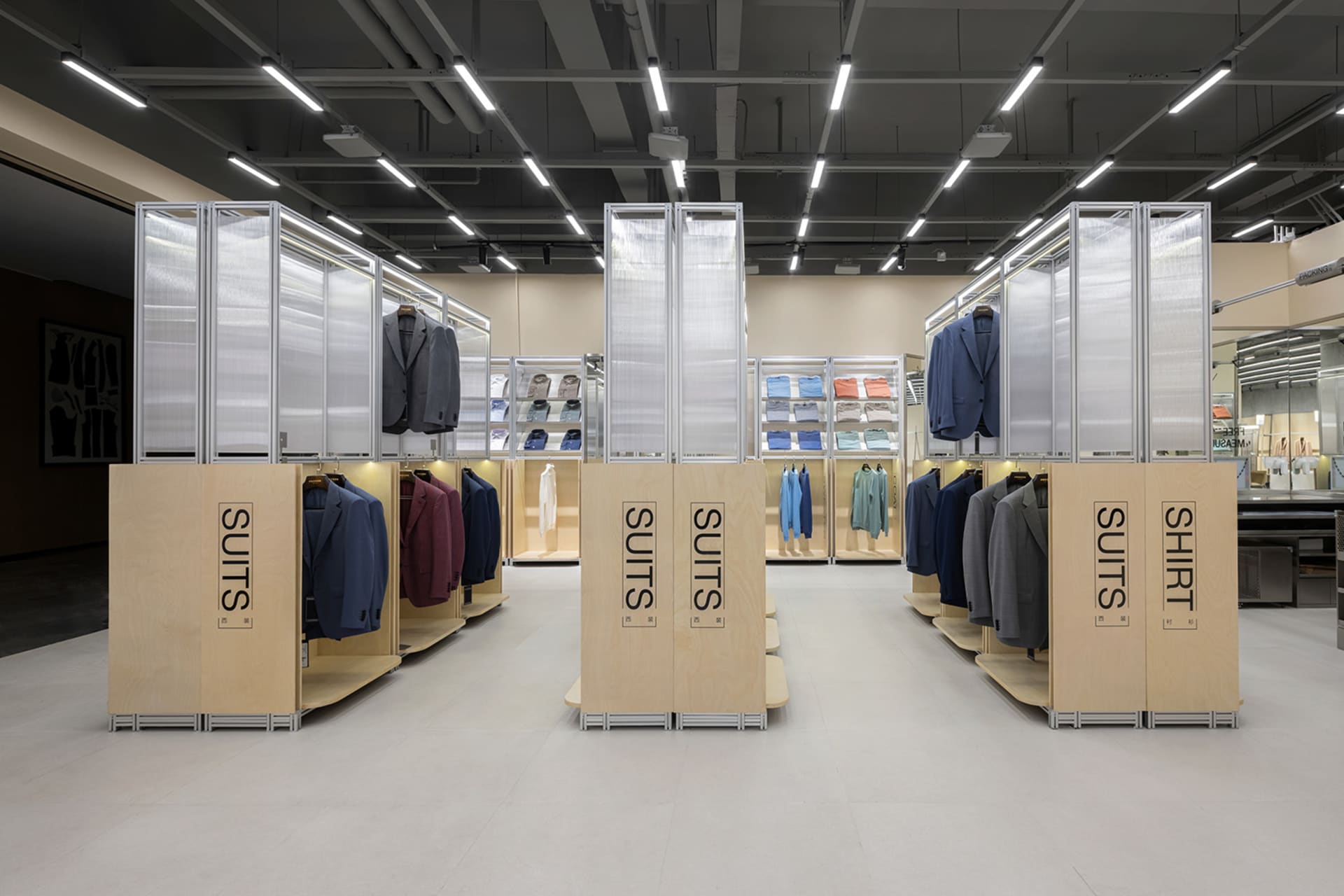 A menswear boutique retail space showcasing suits and shirts on structural steel stands with wooden planks and glass dividers