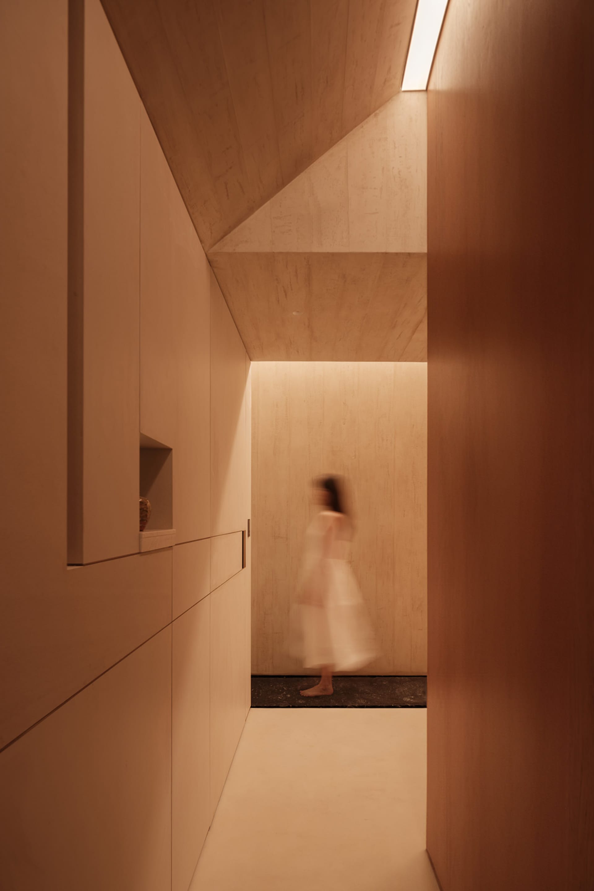 A minimalist residential corridor with concrete walls and wooden flooring.