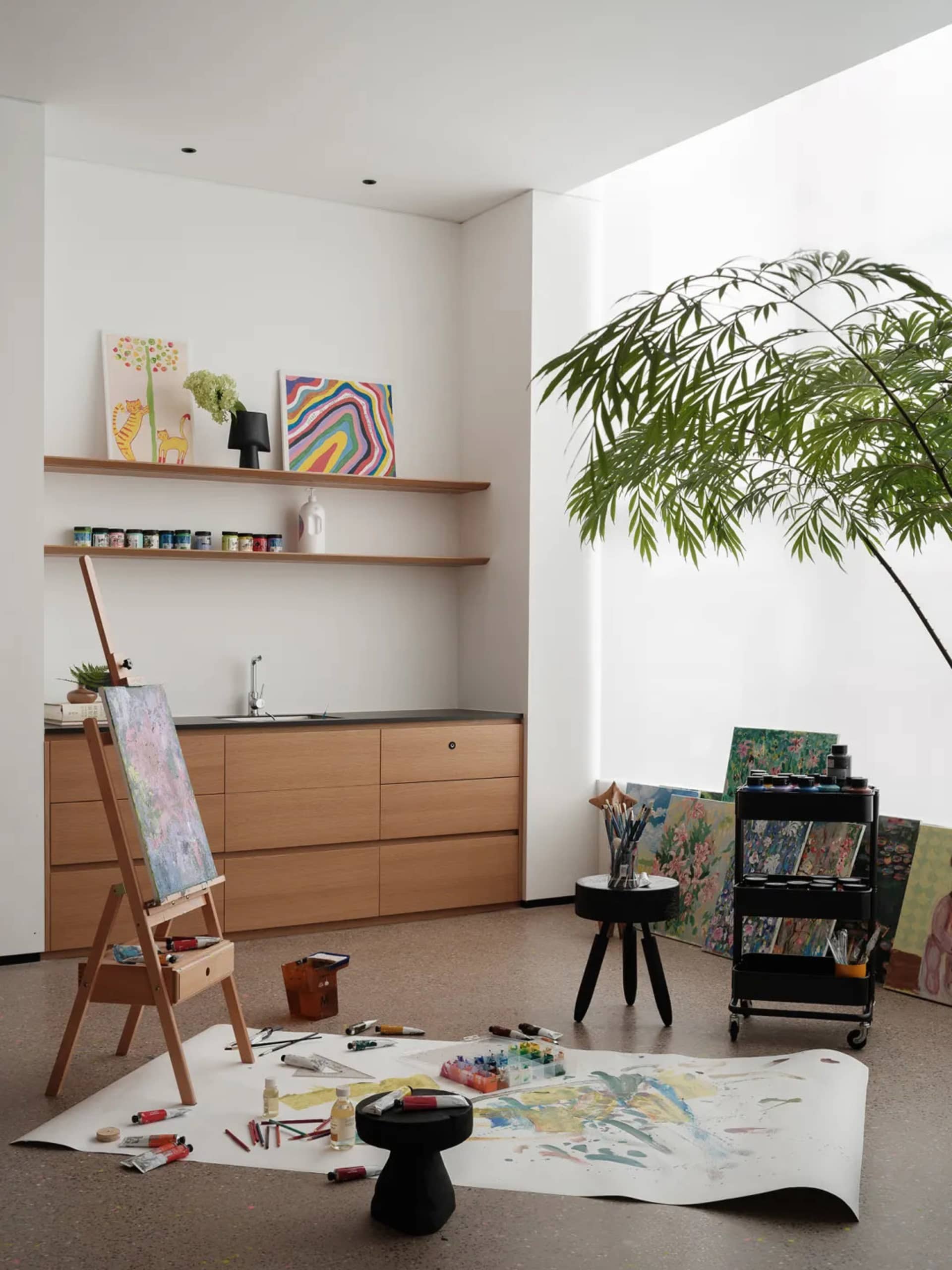 A minimalist painting studio featuring an easel, paints, and paper on the floor.