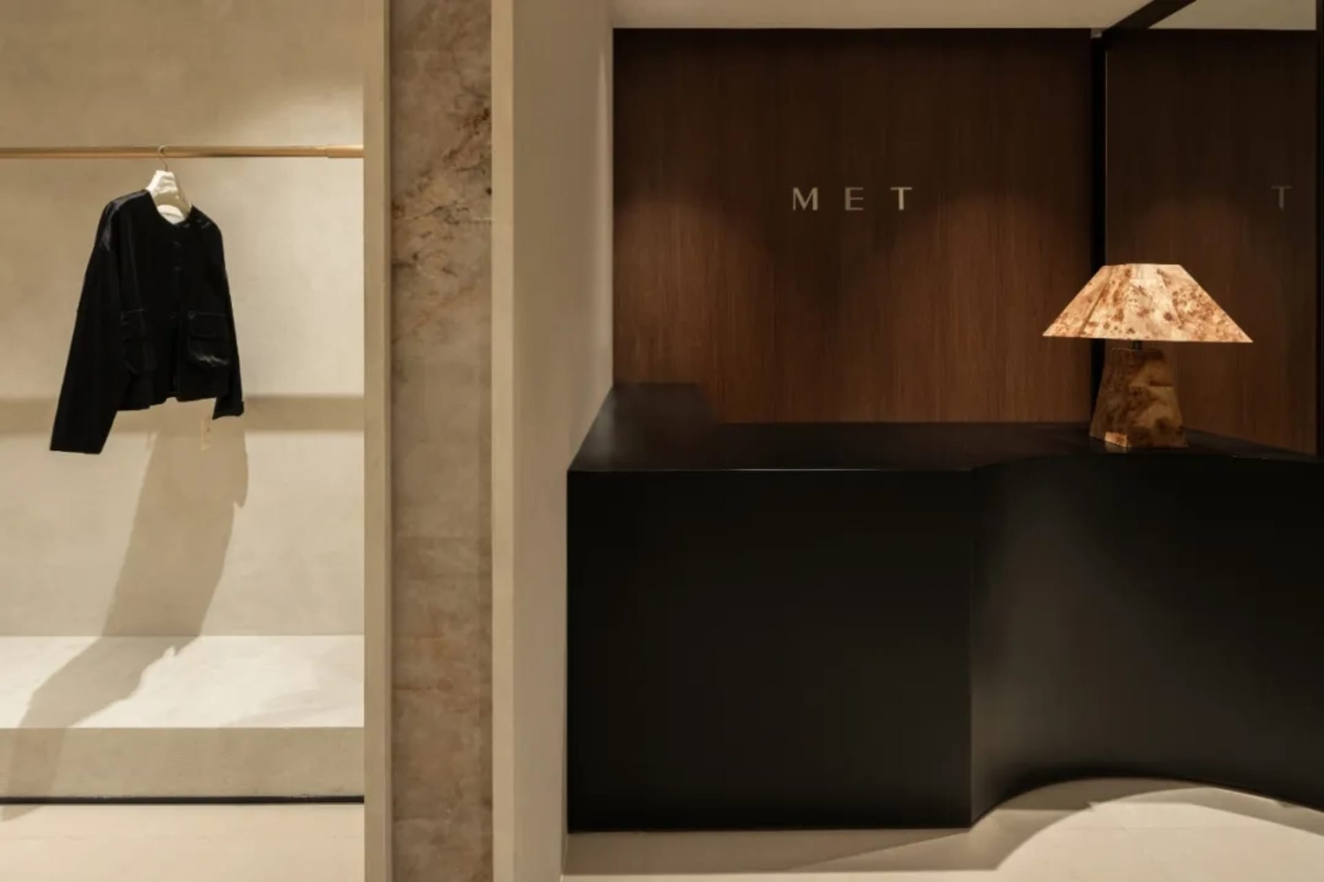 A minimalist shop interior featuring a black counter with a wood lamp, a black leather jacket hanging on a rod, and a marble