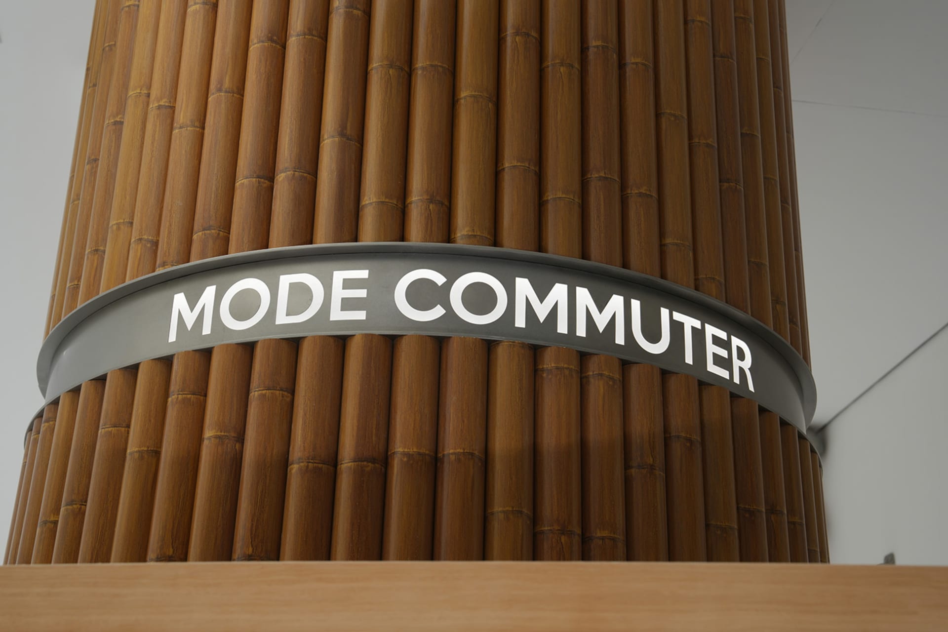 金屬表面上印有「MODE COMMUTER」文字的品牌柱,四周環繞木質面板。
