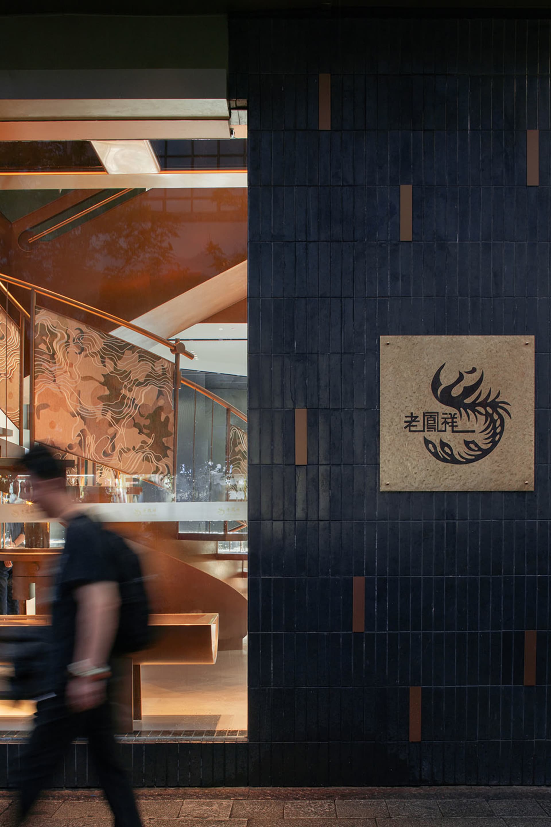 Modern restaurant exterior featuring black tiles and concrete materials, with a branded sign and staircase interior in the ba