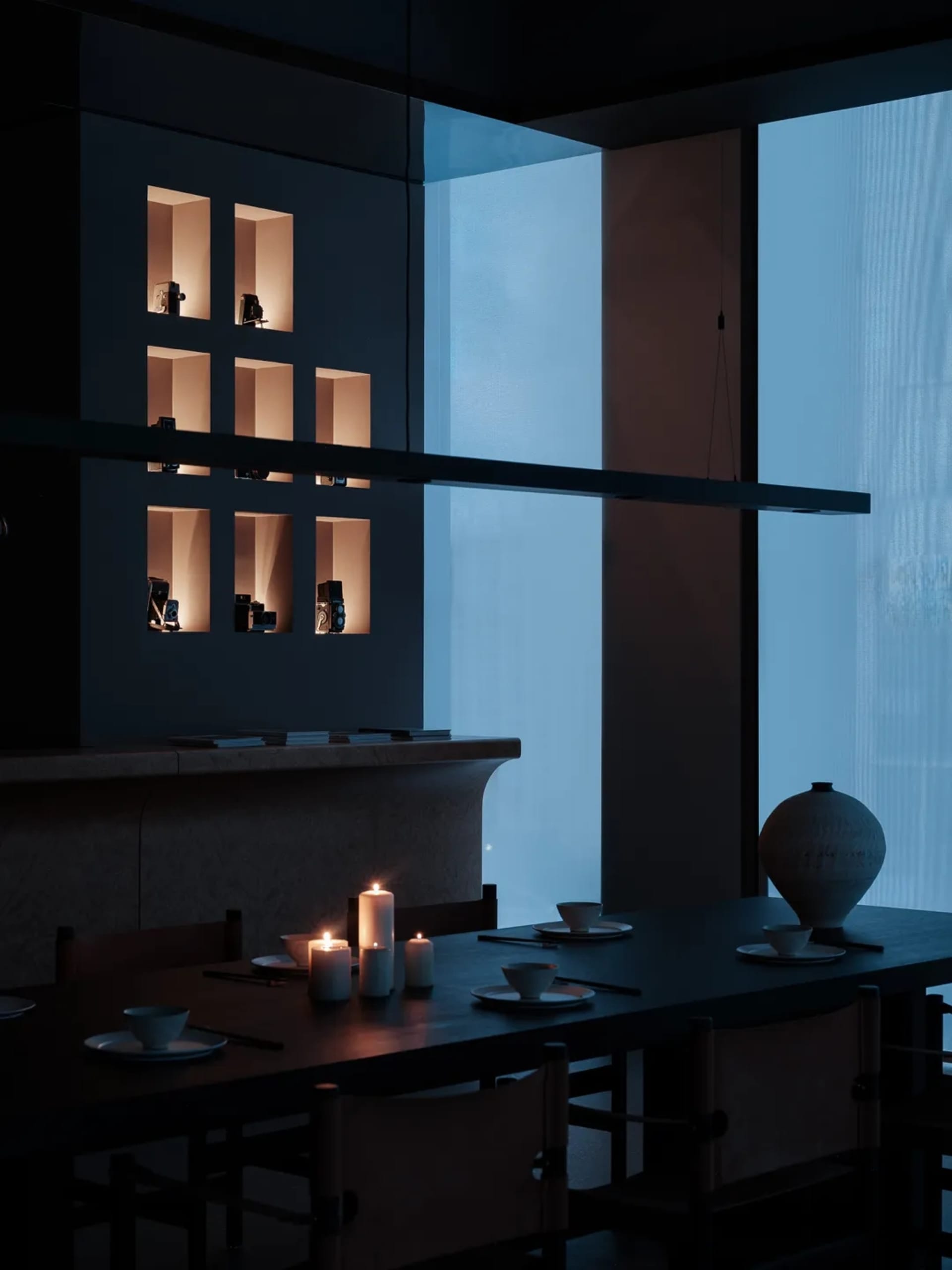 Modern minimalist dining table with glass top and wooden legs surrounded by chairs, featuring a wall display of illuminated v