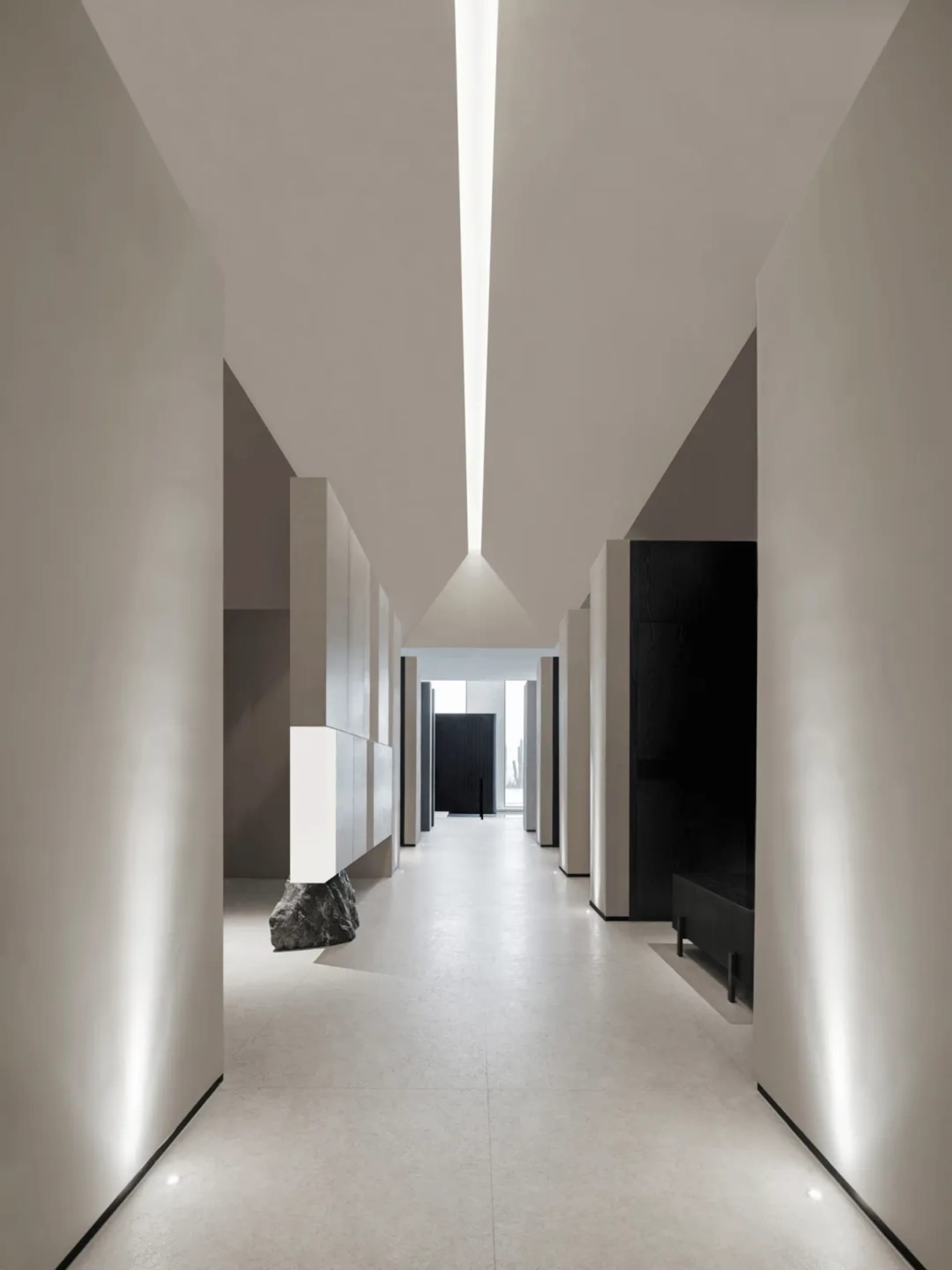 A minimalist modern corridor with concrete walls and floor, featuring a large rock centerpiece.