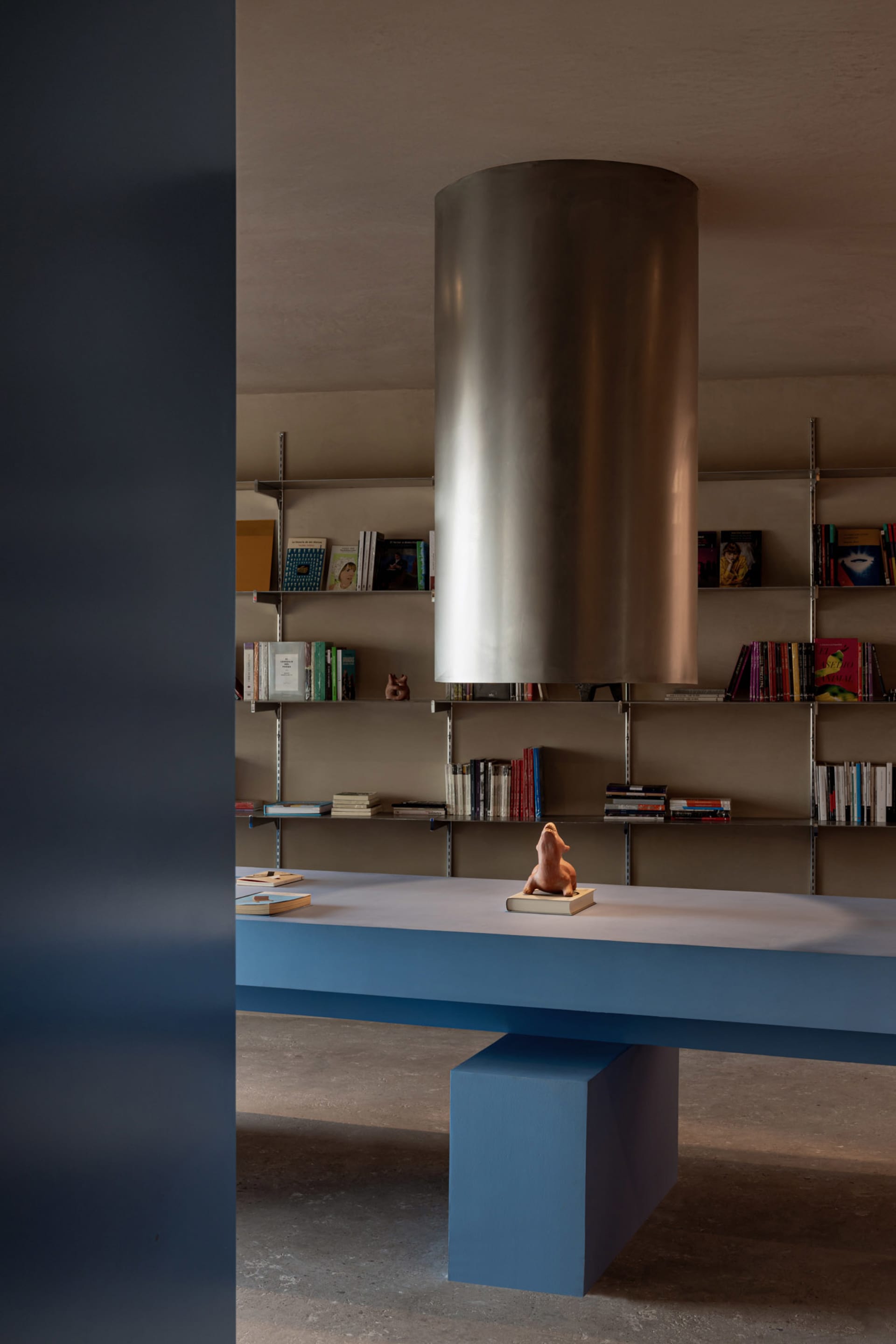 A minimalist room with a blue and metallic bookshelf, featuring a sculpture of a lion on a book.