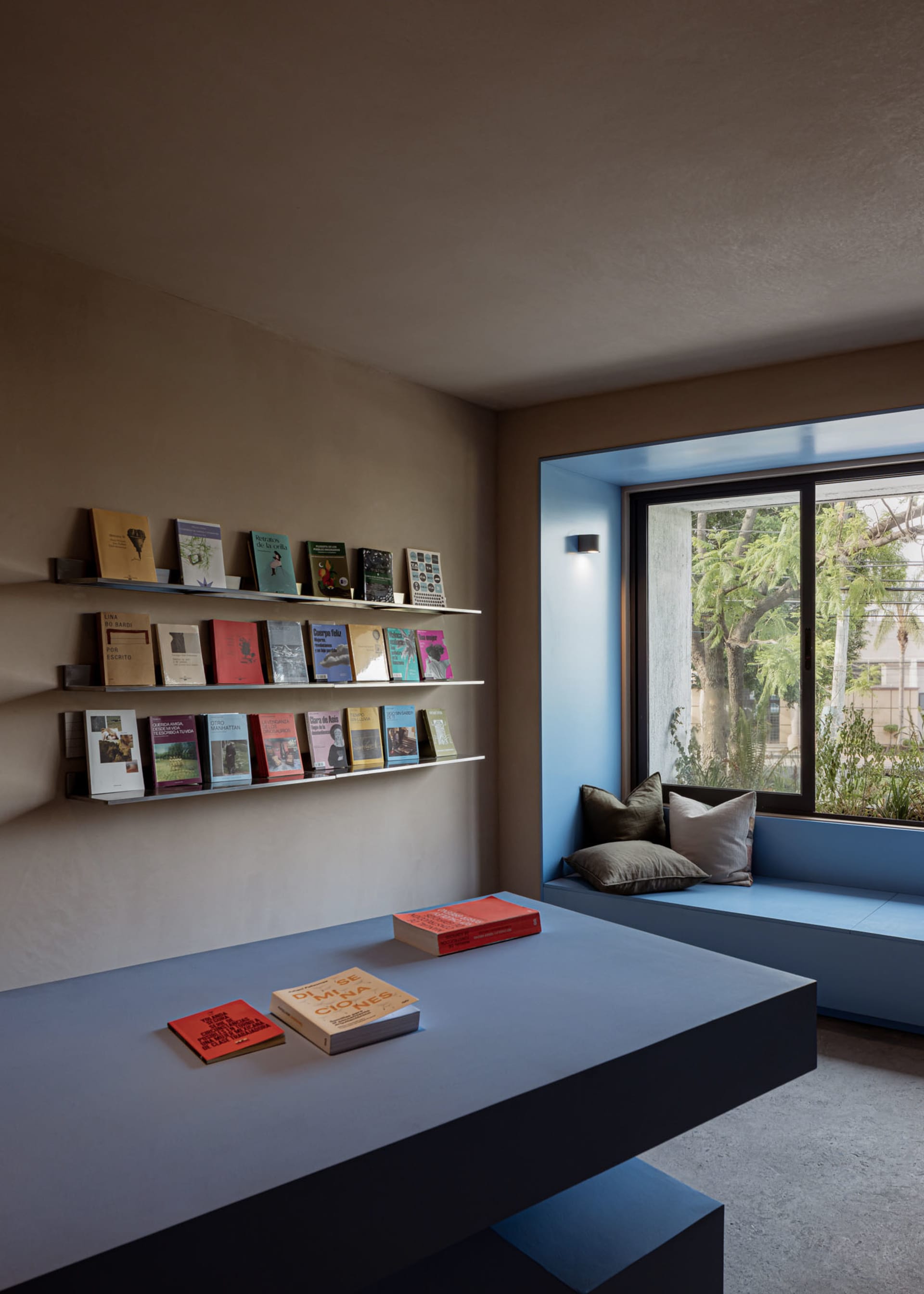 A minimalist library room with concrete walls, floating shelves, and a built-in bench seat.