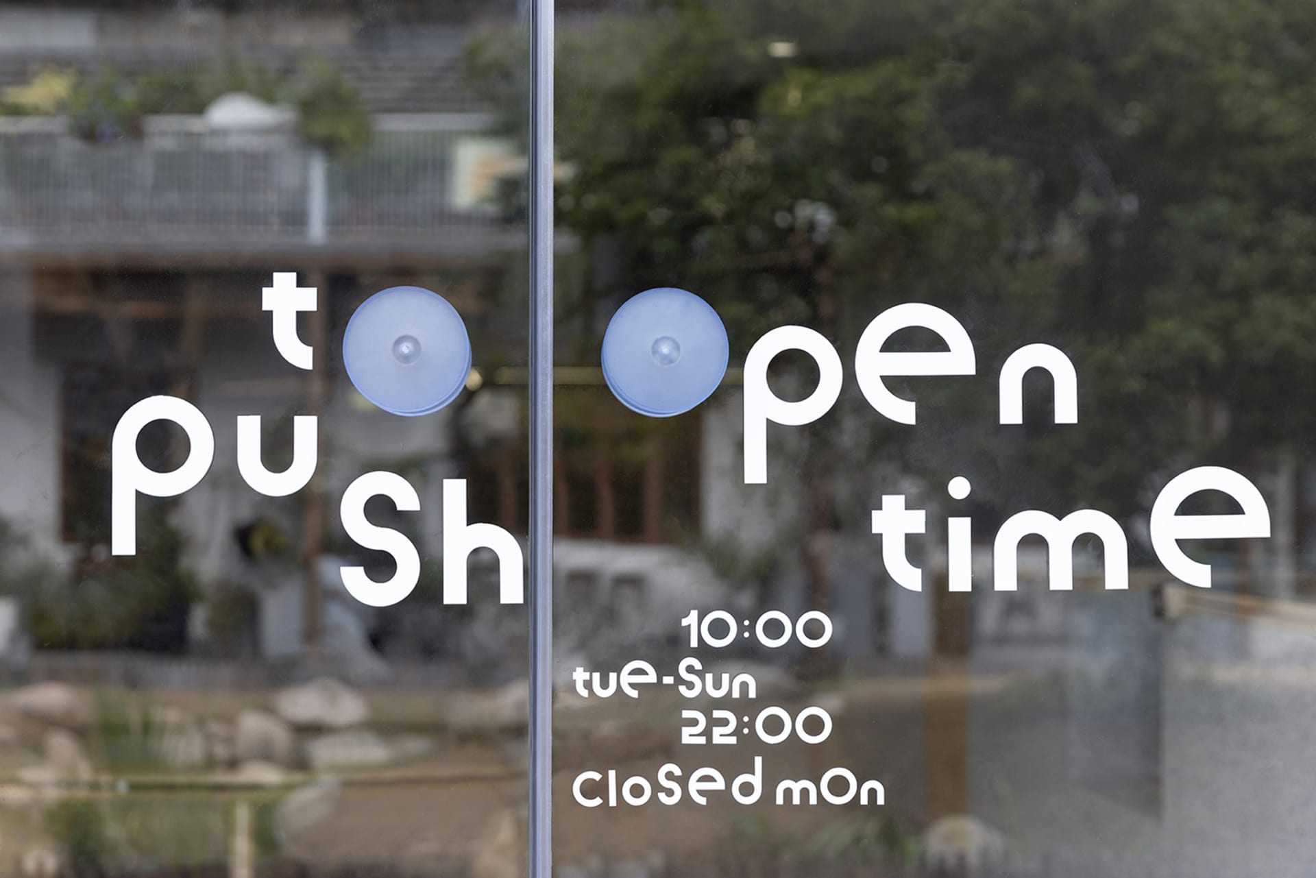A glass storefront window with instructions to push to open, operating times, and days of closure.