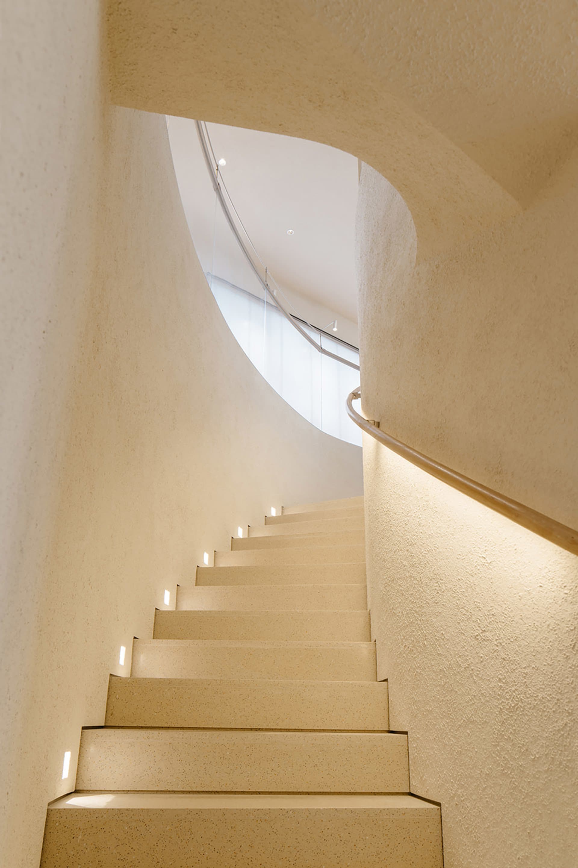 A modern staircase with concrete steps and walls, illuminated with small lights on the risers.