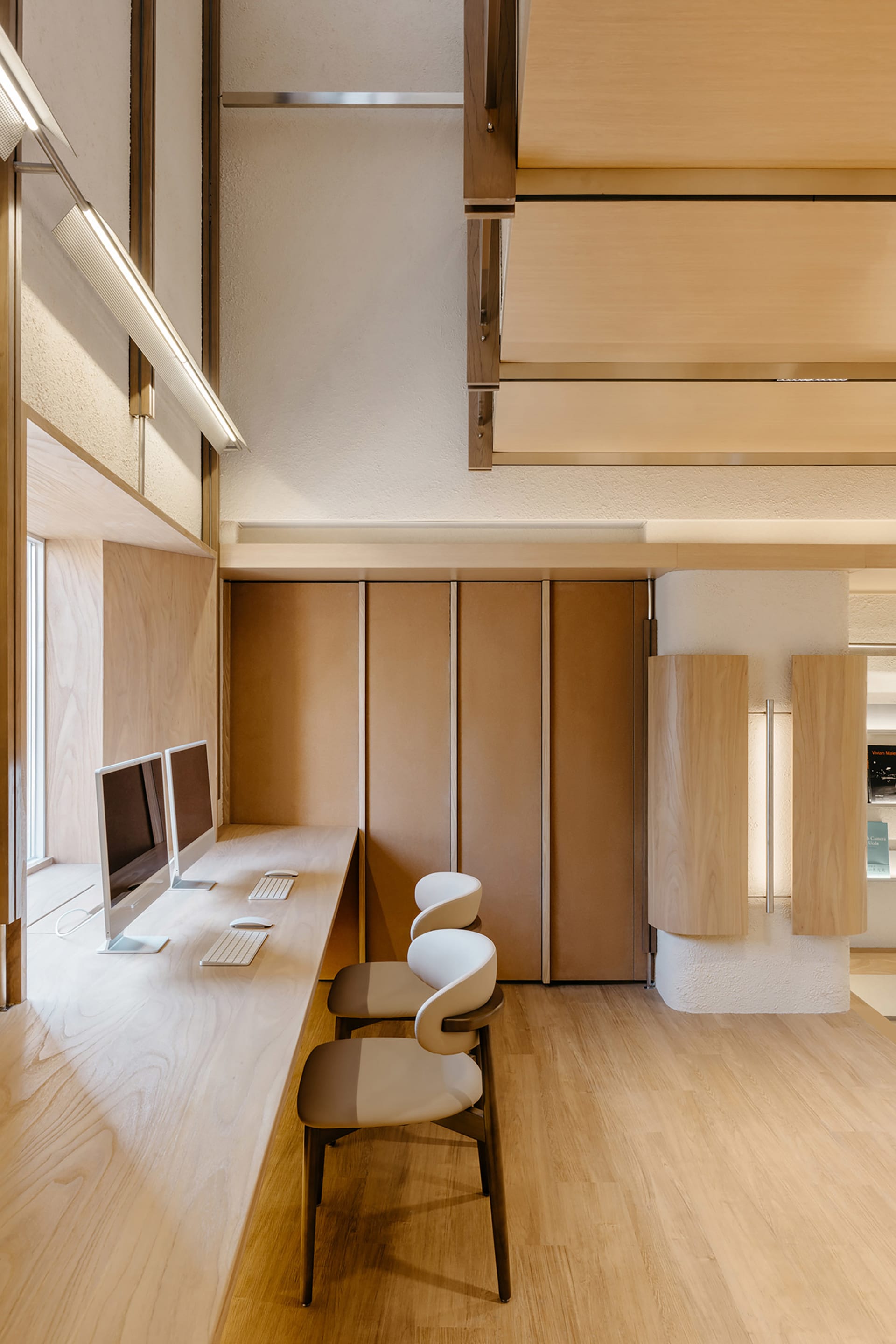 Modern office interior with wooden furniture, featuring a sleek desk setup and ergonomic chairs.