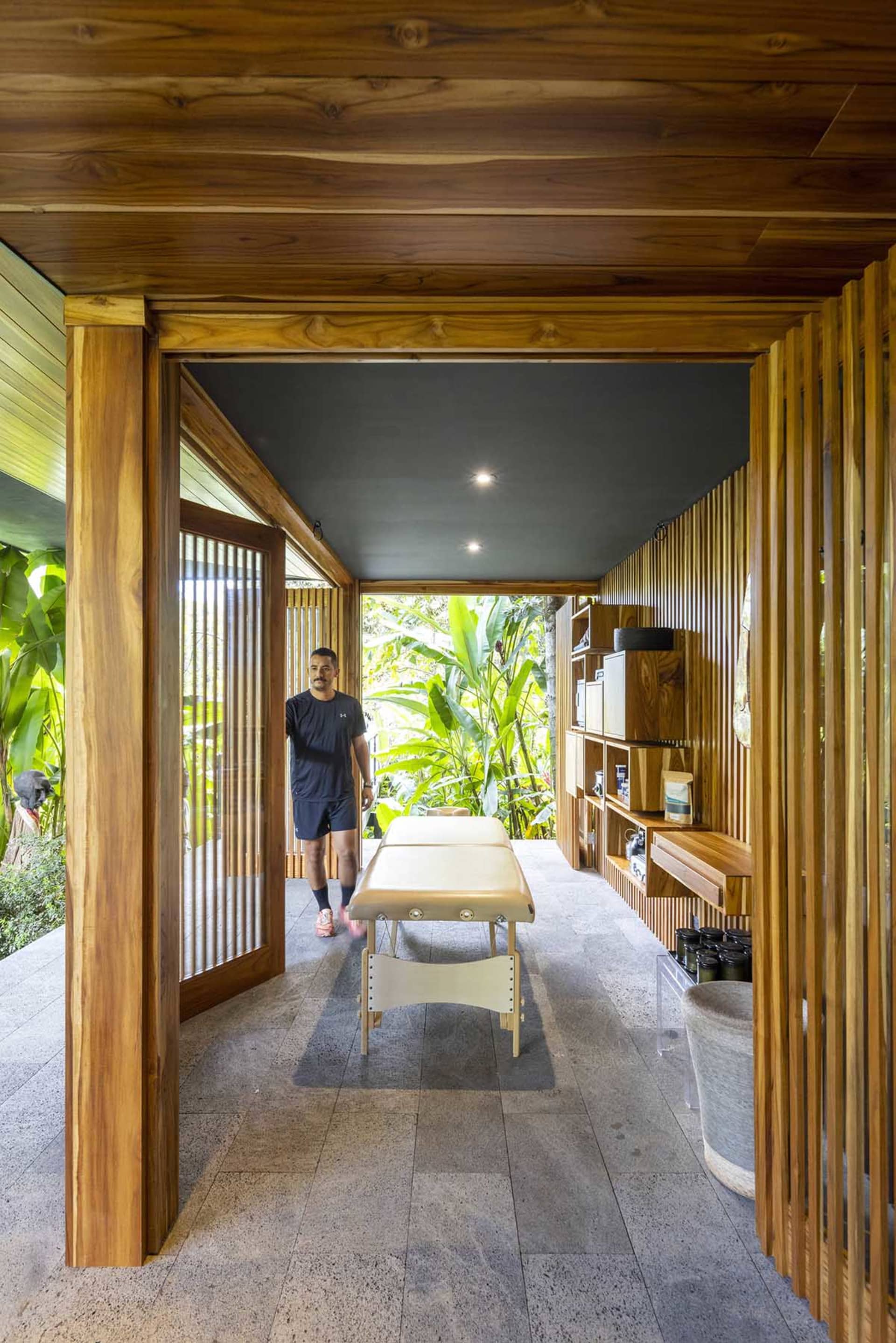 A person walking into a wooden spa treatment room with a massage table and shelves.