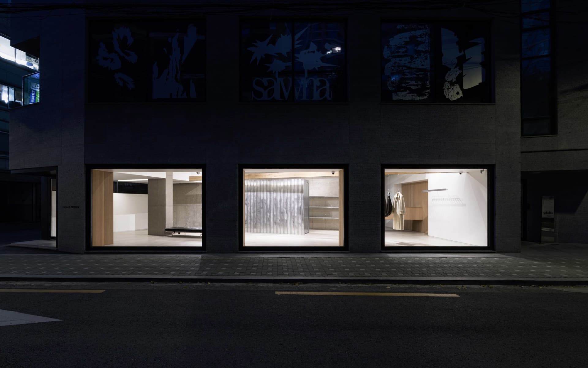 A modern retail storefront illuminated from within at night, showcasing minimalist design elements and metal window displays.