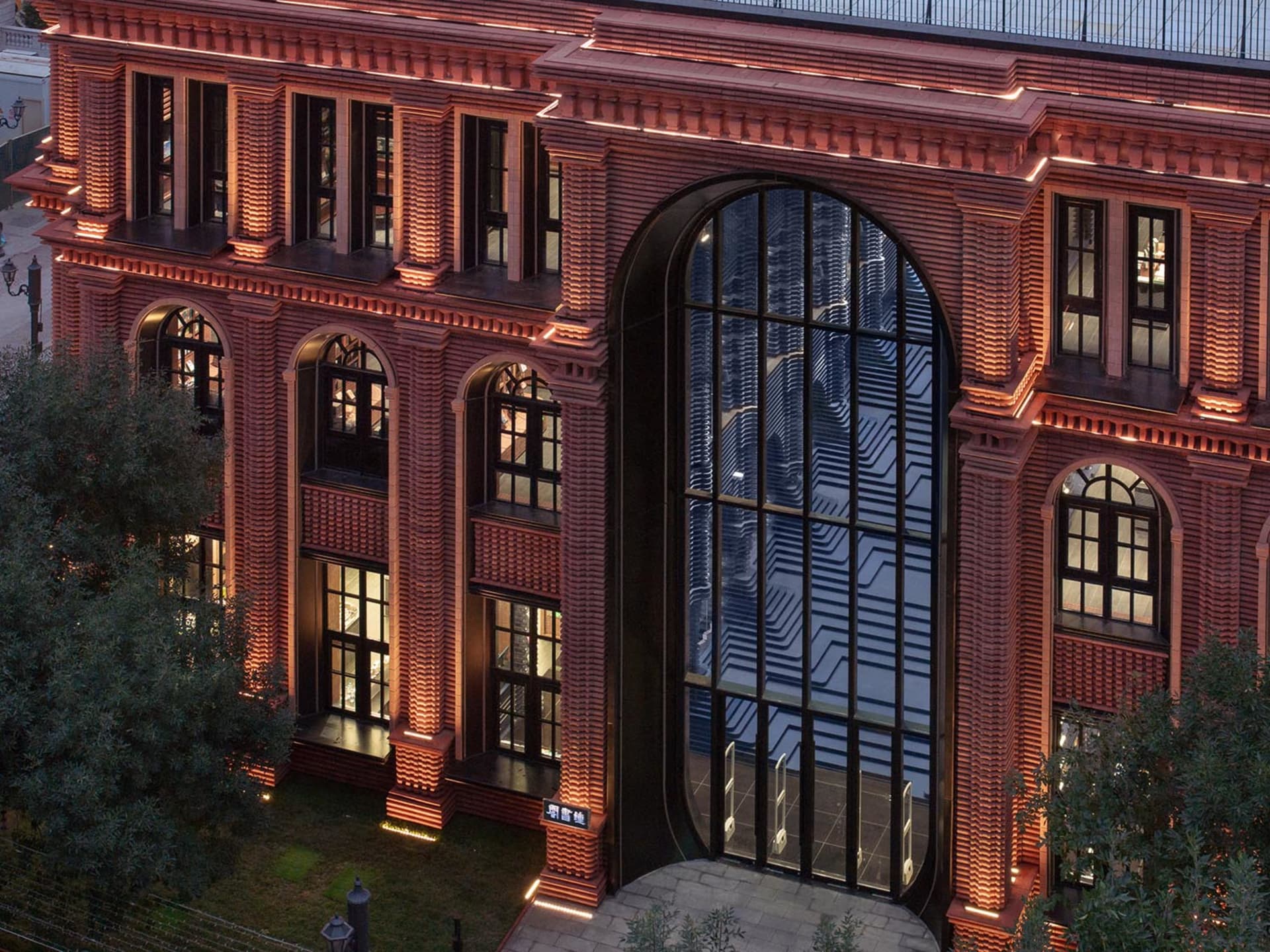 The exterior of a brick building illuminated at night, featuring arched windows and a large glass entrance.