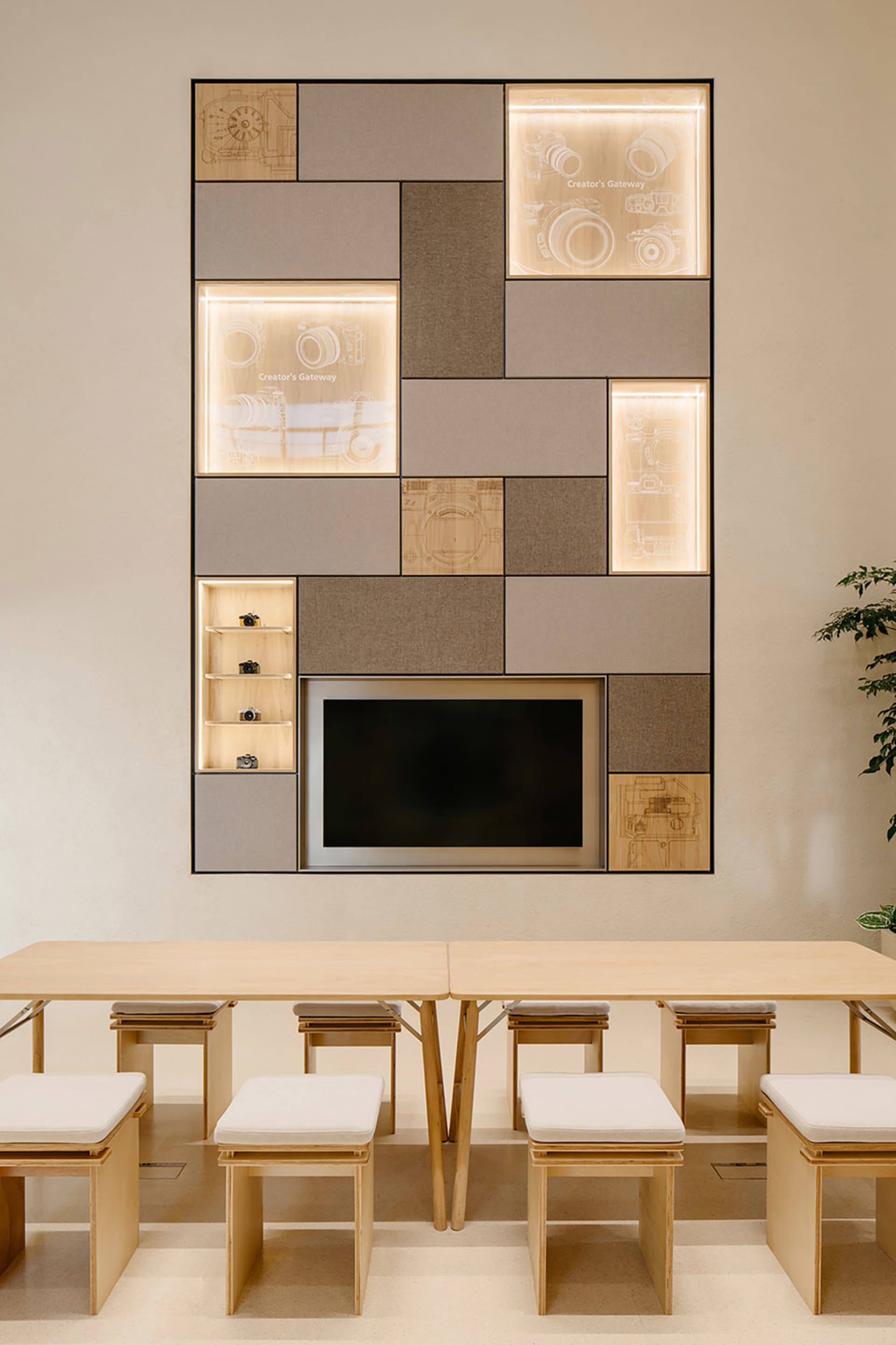 A co-working space with a modern interior design featuring wooden tables and chairs, fabric-covered benches, and glass elemen