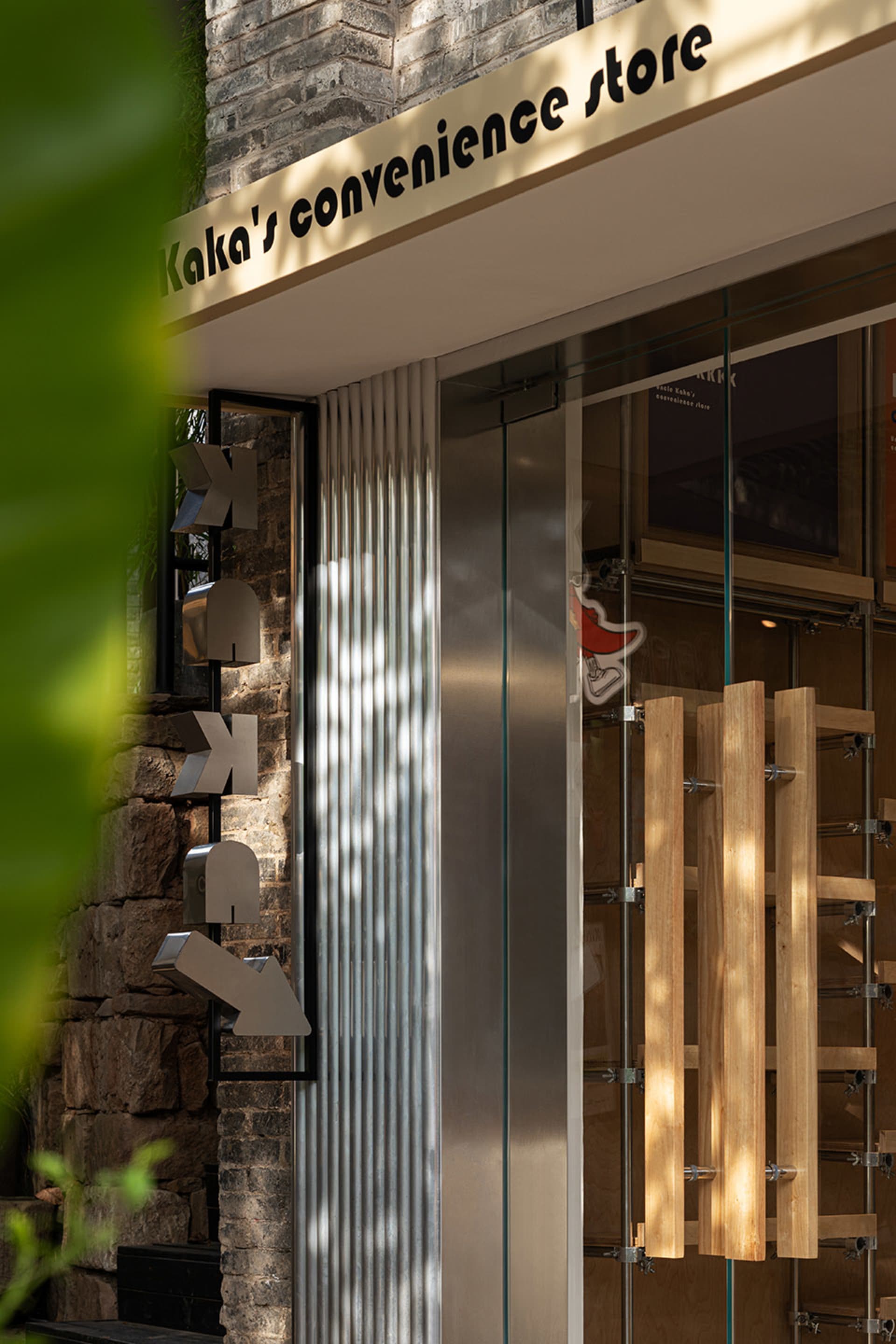 現代店面玻璃門,搭配木製把手與金屬框,背景為石牆與綠葉。