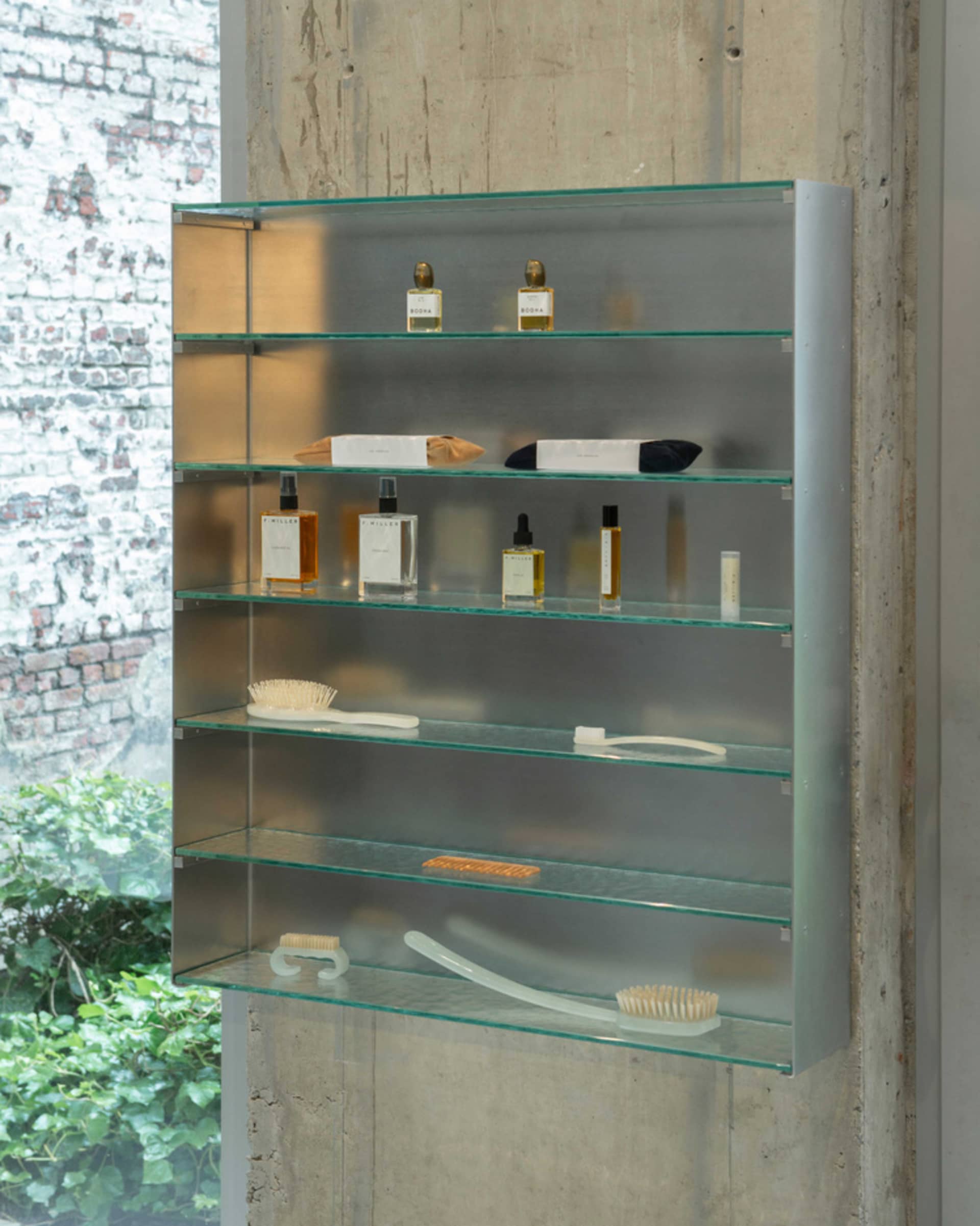 Glass and metal industrial-style shelf displaying various products, including bottles, brushes, and a toothbrush.