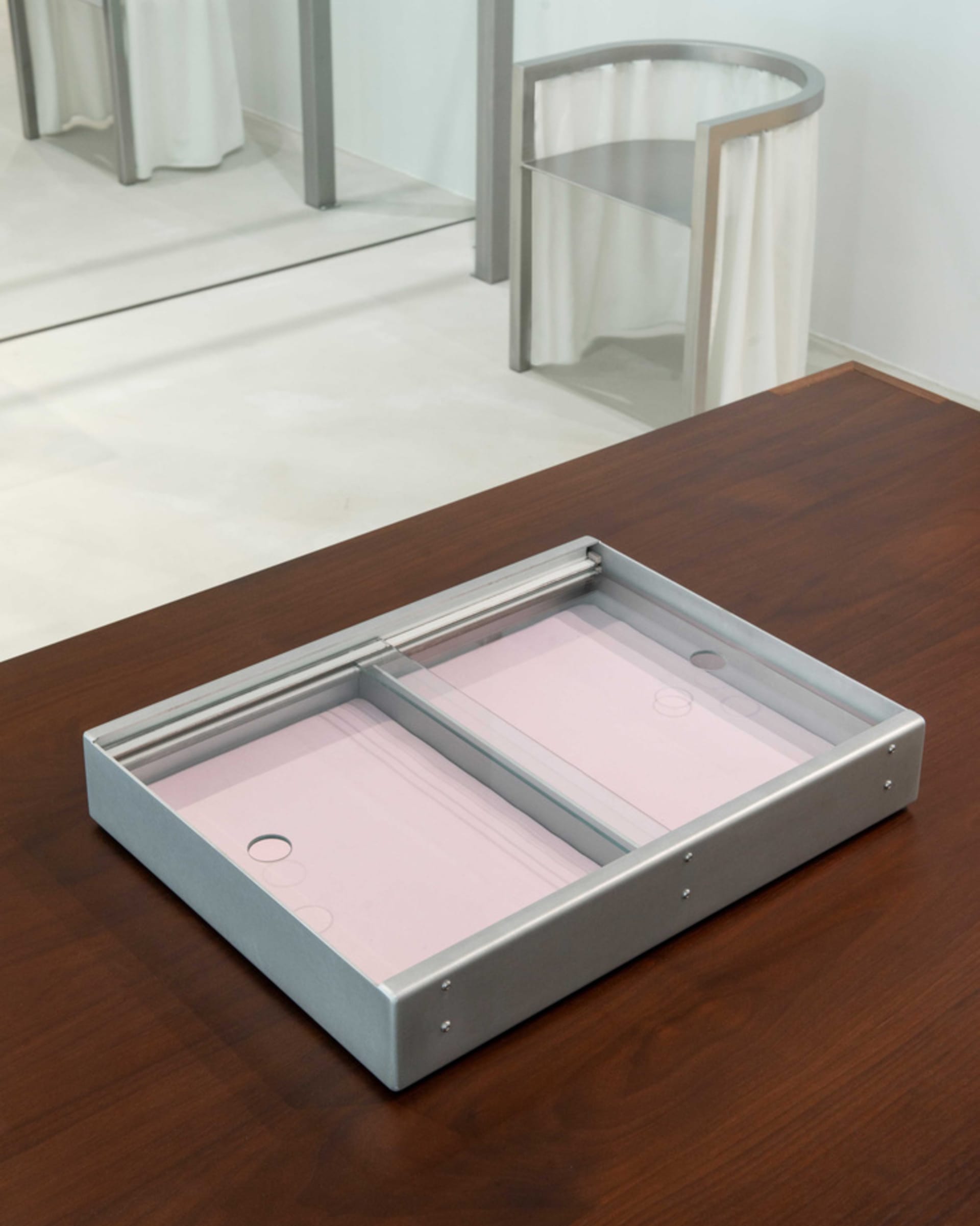 A metal rectangular product bin with pink sheets inside, placed on a wooden table.