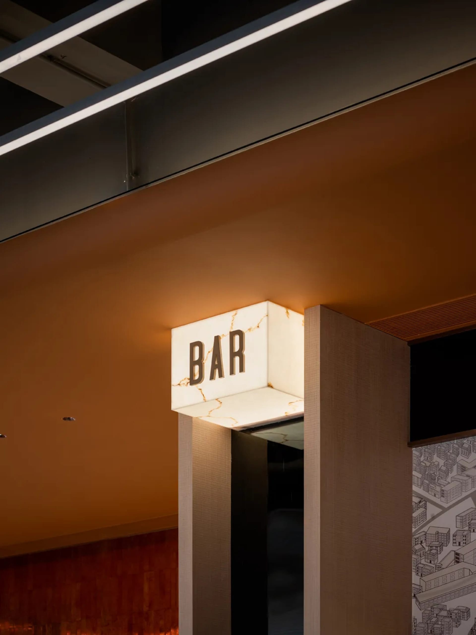 在極簡工業風室內空間中，一塊金屬材質的照明招牌顯示著「BAR」字樣。