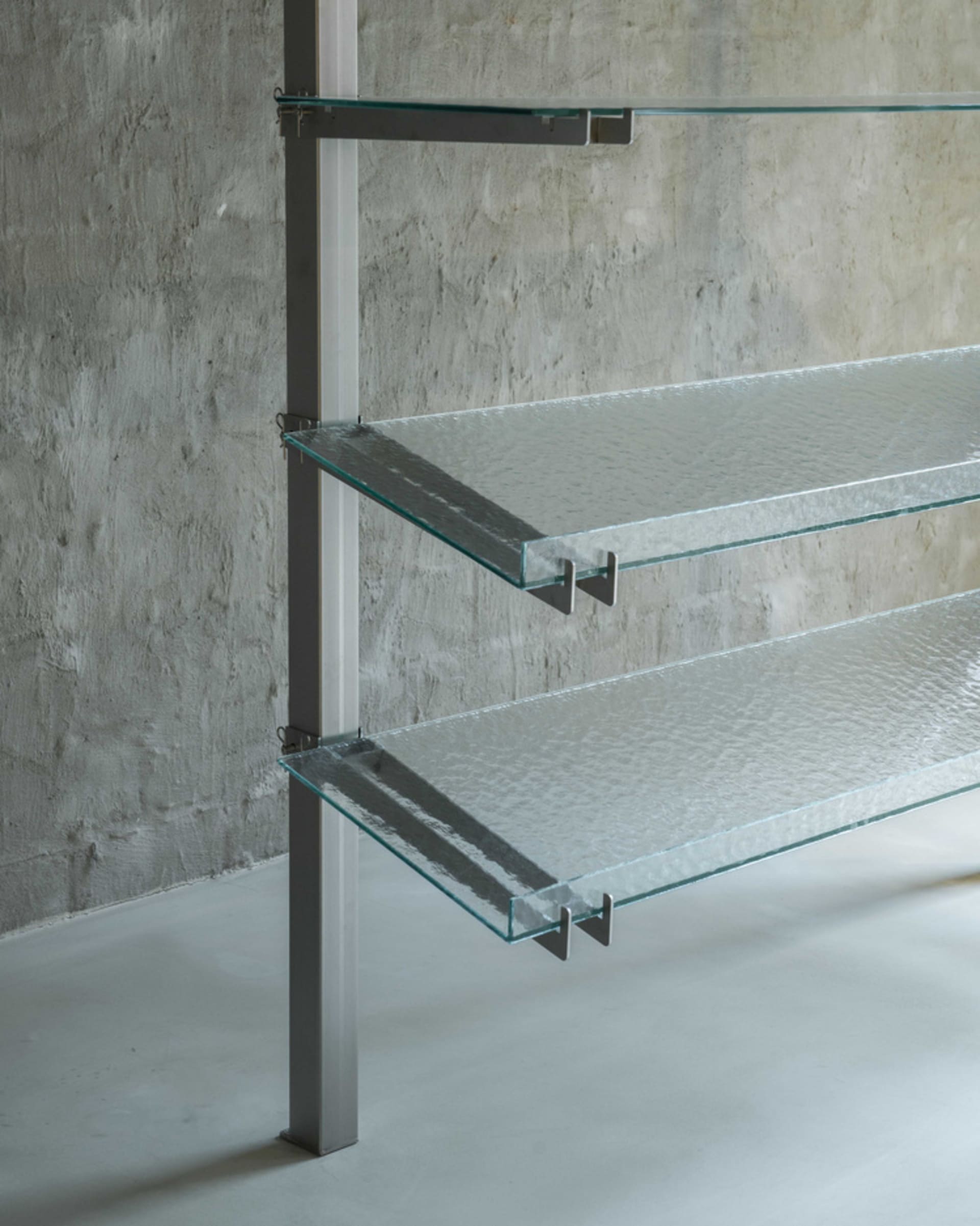 A minimalist glass shelf rack mounted on a concrete wall, featuring transparent glass shelves.