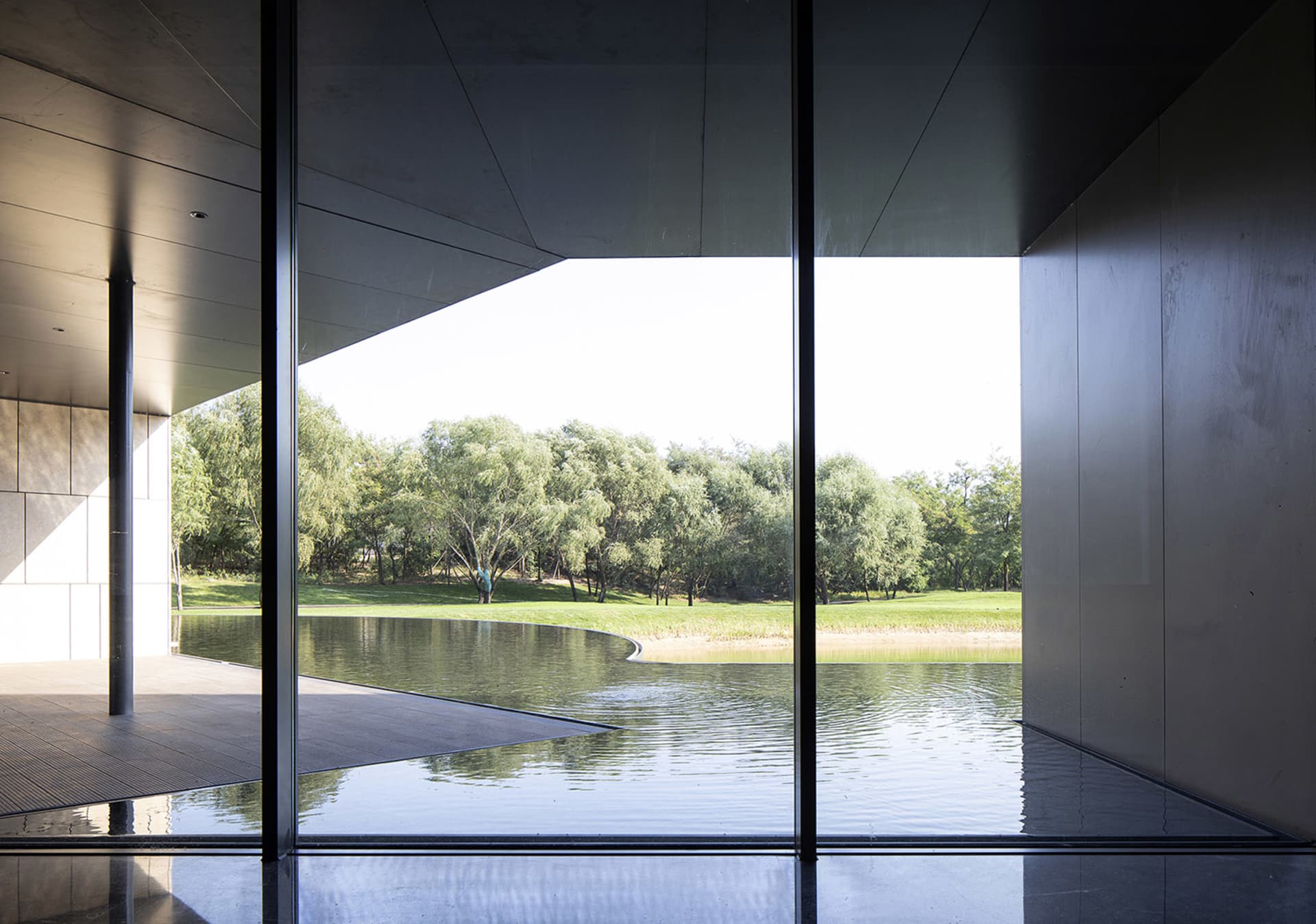 Modern building with glass walls overlooking a serene lake surrounded by greenery.