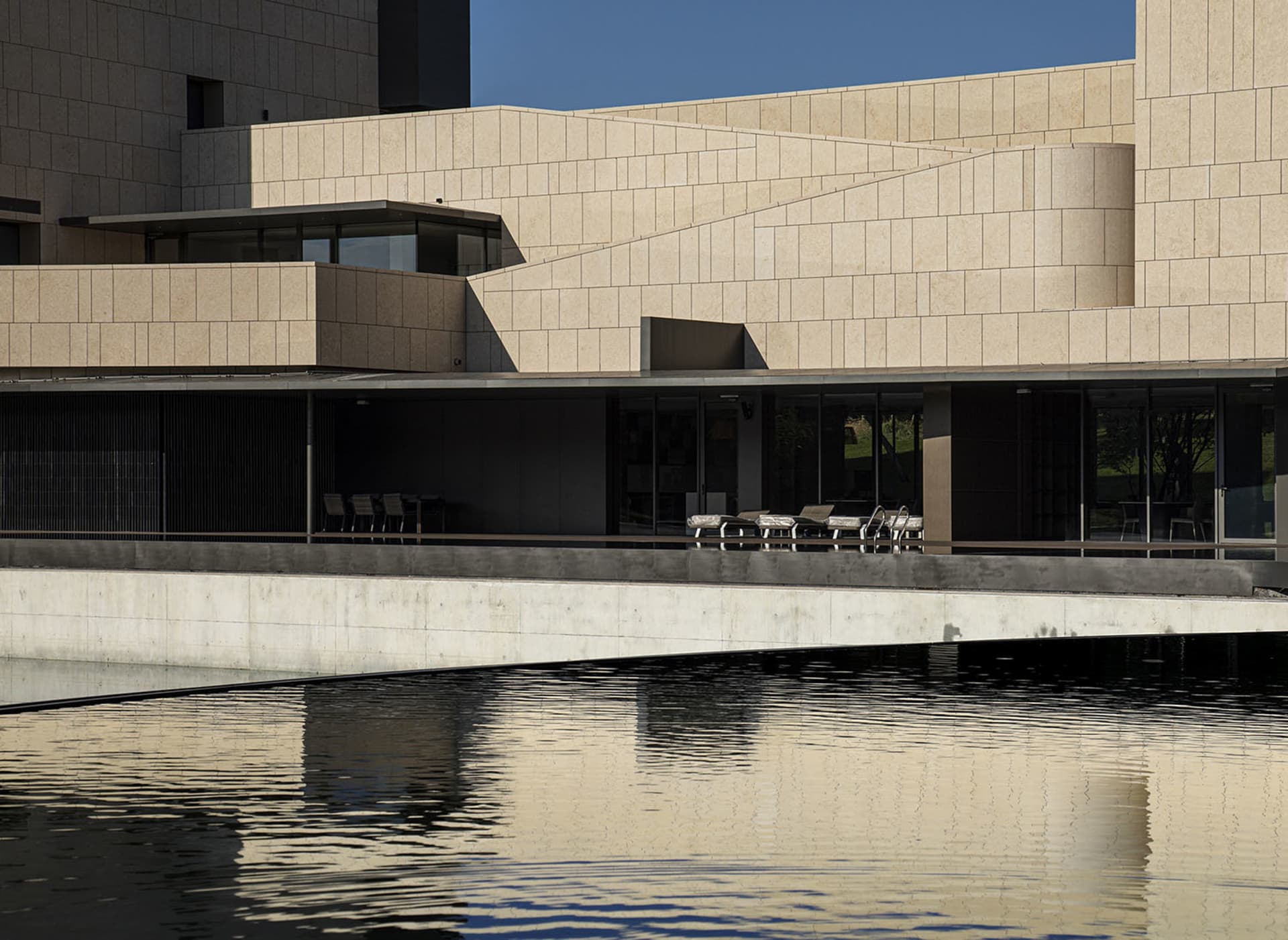 A modern public building with concrete and glass surfaces reflected in water.