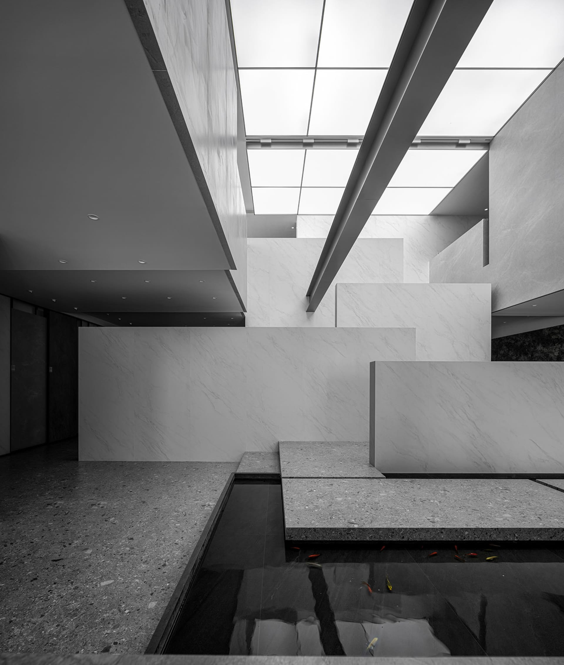 Modern interior design featuring a minimalist lobby with concrete and glass materials, illuminated by overhead lighting.