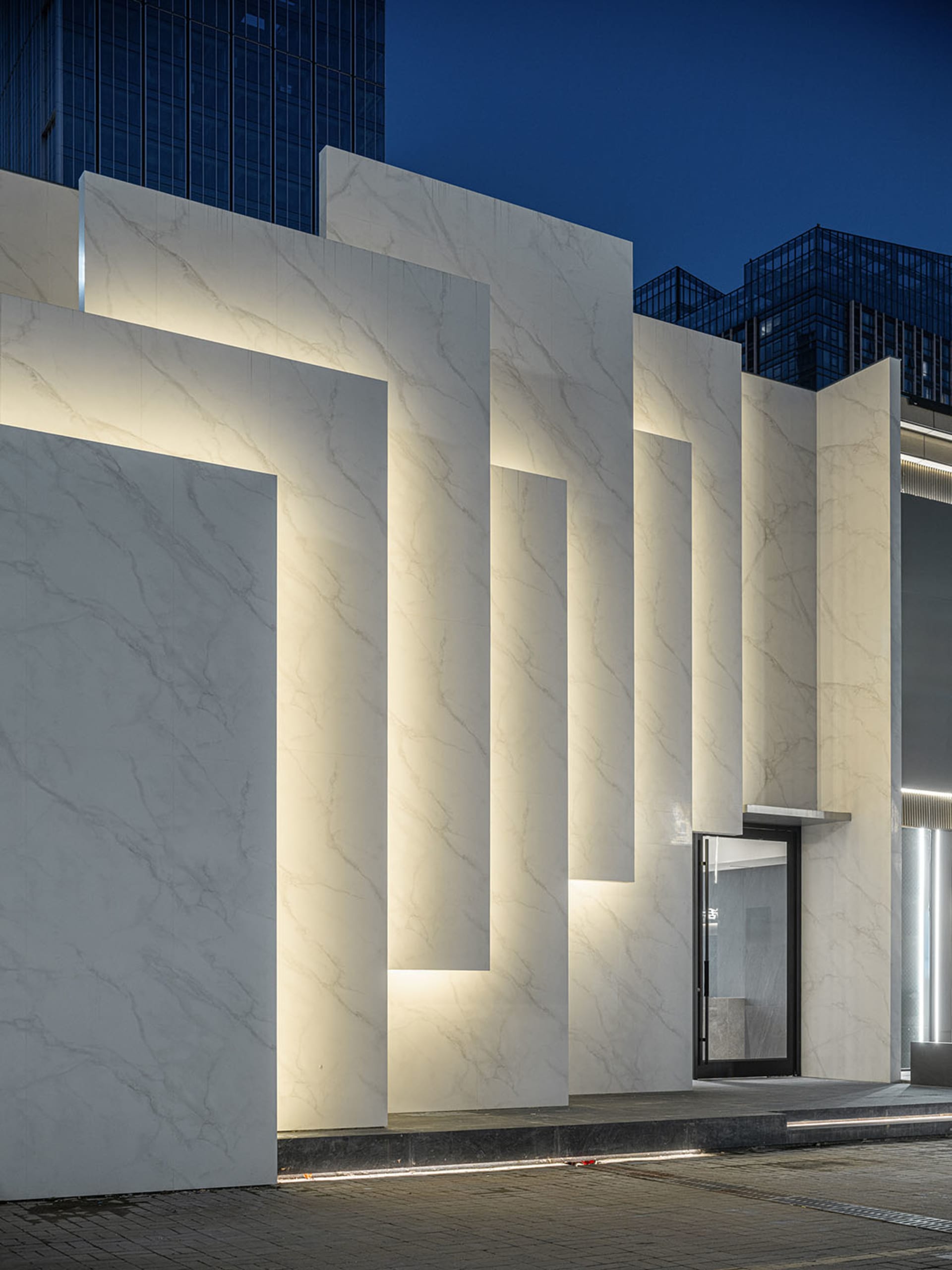 Modern storefront with illuminated marble columns at night.